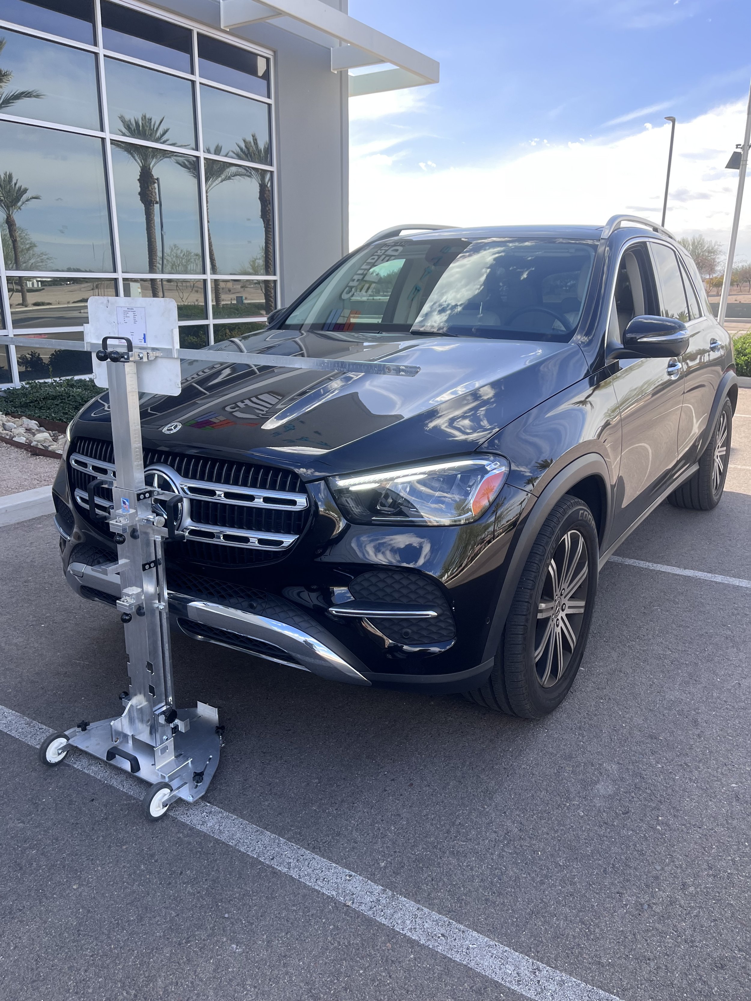 A black Mercedes-Benz SUV parked in a lot, with a metal device attached to its front, used for vehicle testing or calibration.