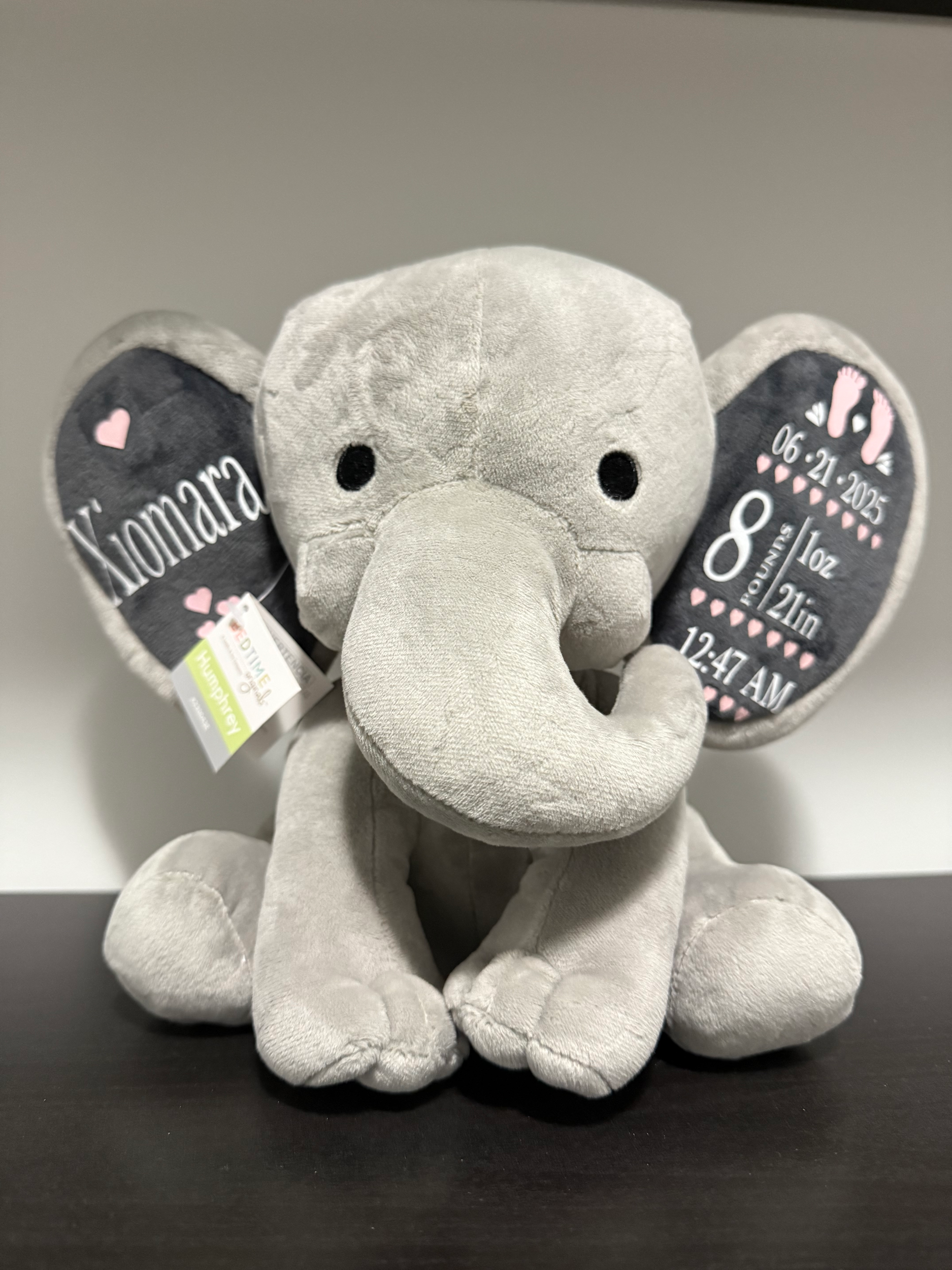 A plush gray elephant with decorative ears displaying birth information, including name 'Hannah,' date '06.21.2023,' weight '8 lbs 1 oz,' length '21 inches,' and time '12:47 AM.'