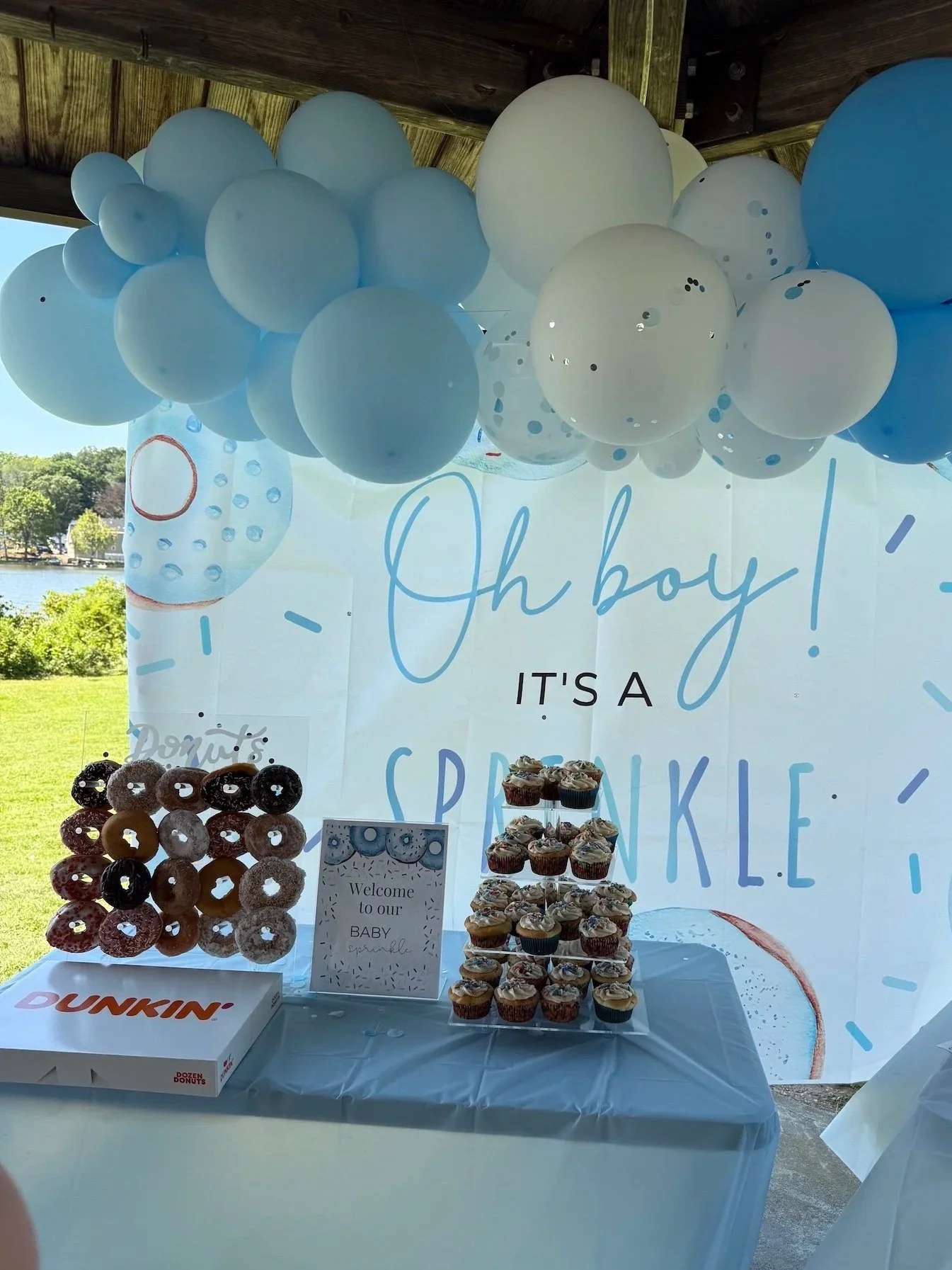 Baby shower dessert table with cupcakes, donuts, and balloons, celebrating a baby boy with a spring theme.