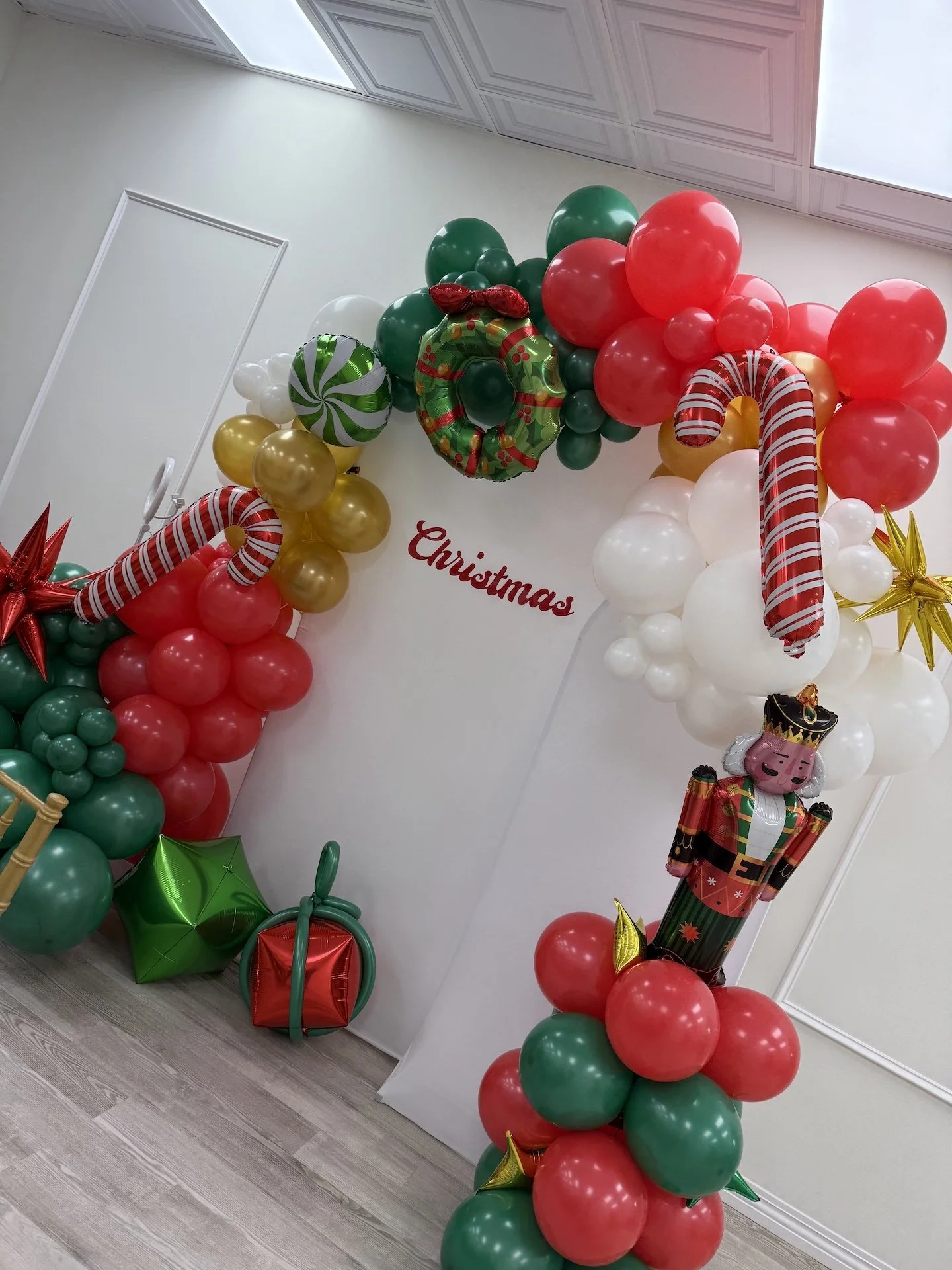 Christmas balloon decoration with red, green, white, and gold balloons, including candy cane and wreath designs, a Nutcracker figure, and a