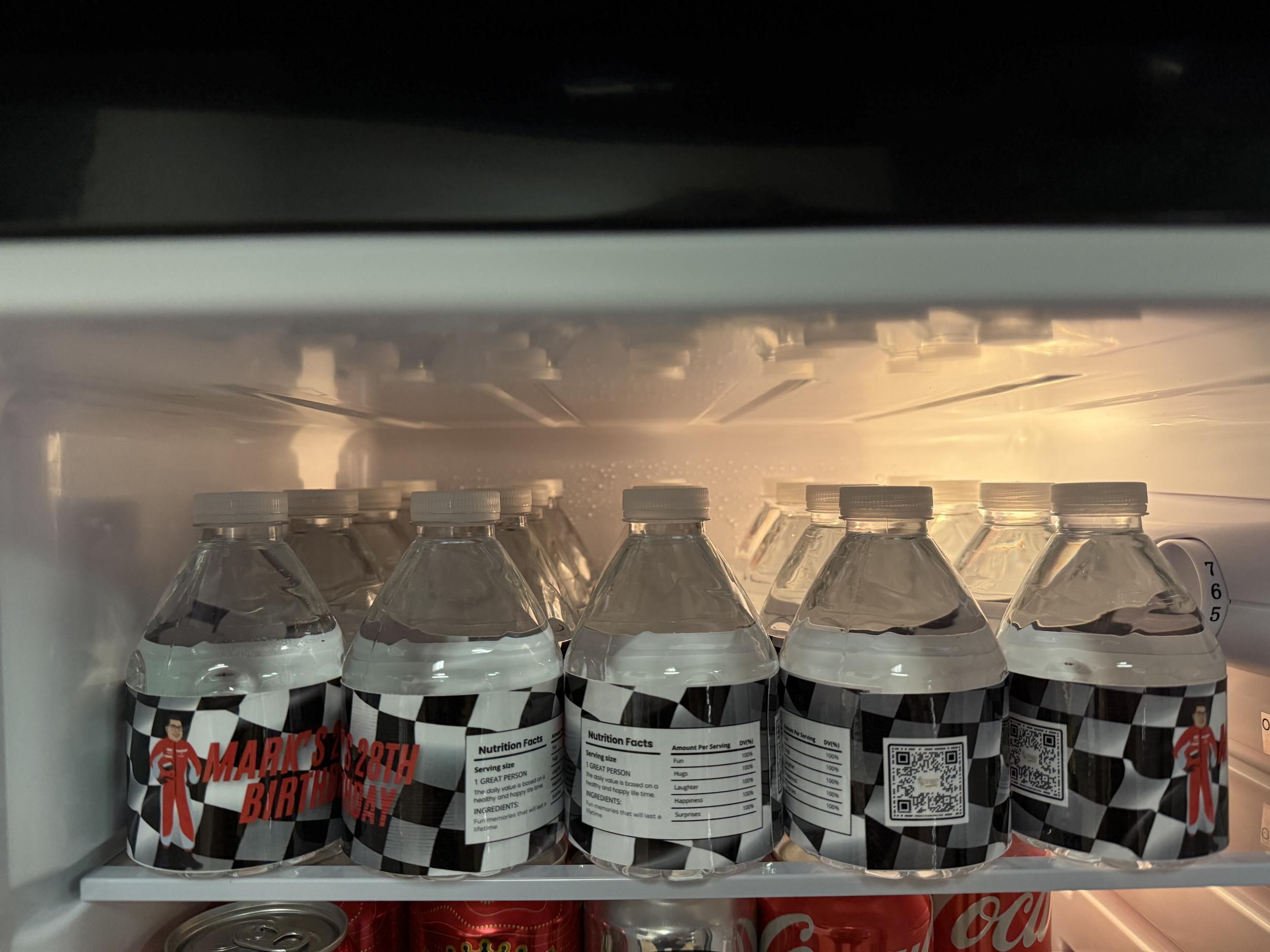 Bottles with racing checkered pattern labels and birthday message inside a refrigerator.