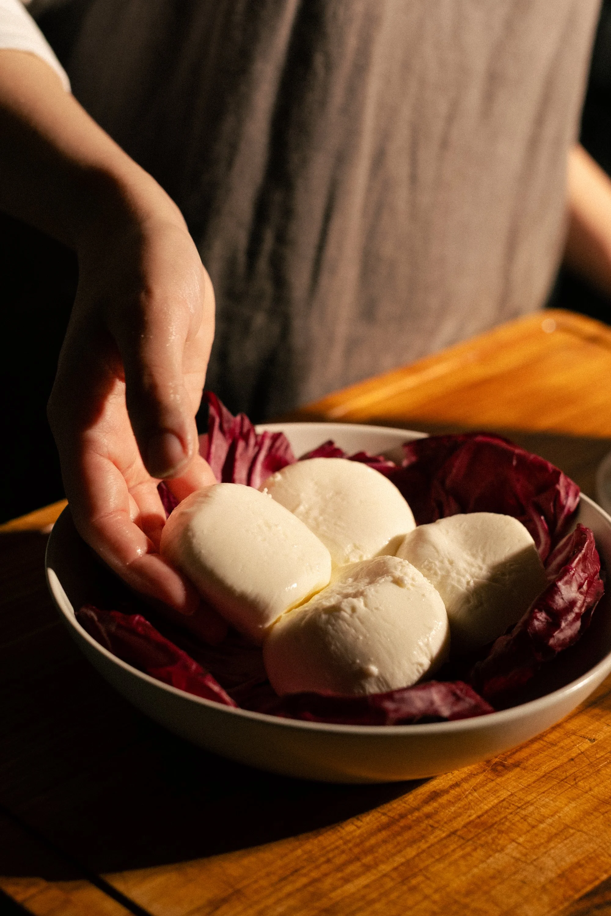 A bowl of fresh mozzarella cheese balls seasoned with olive oil and herbs, garnished with red leaf lettuce, on a wooden table.