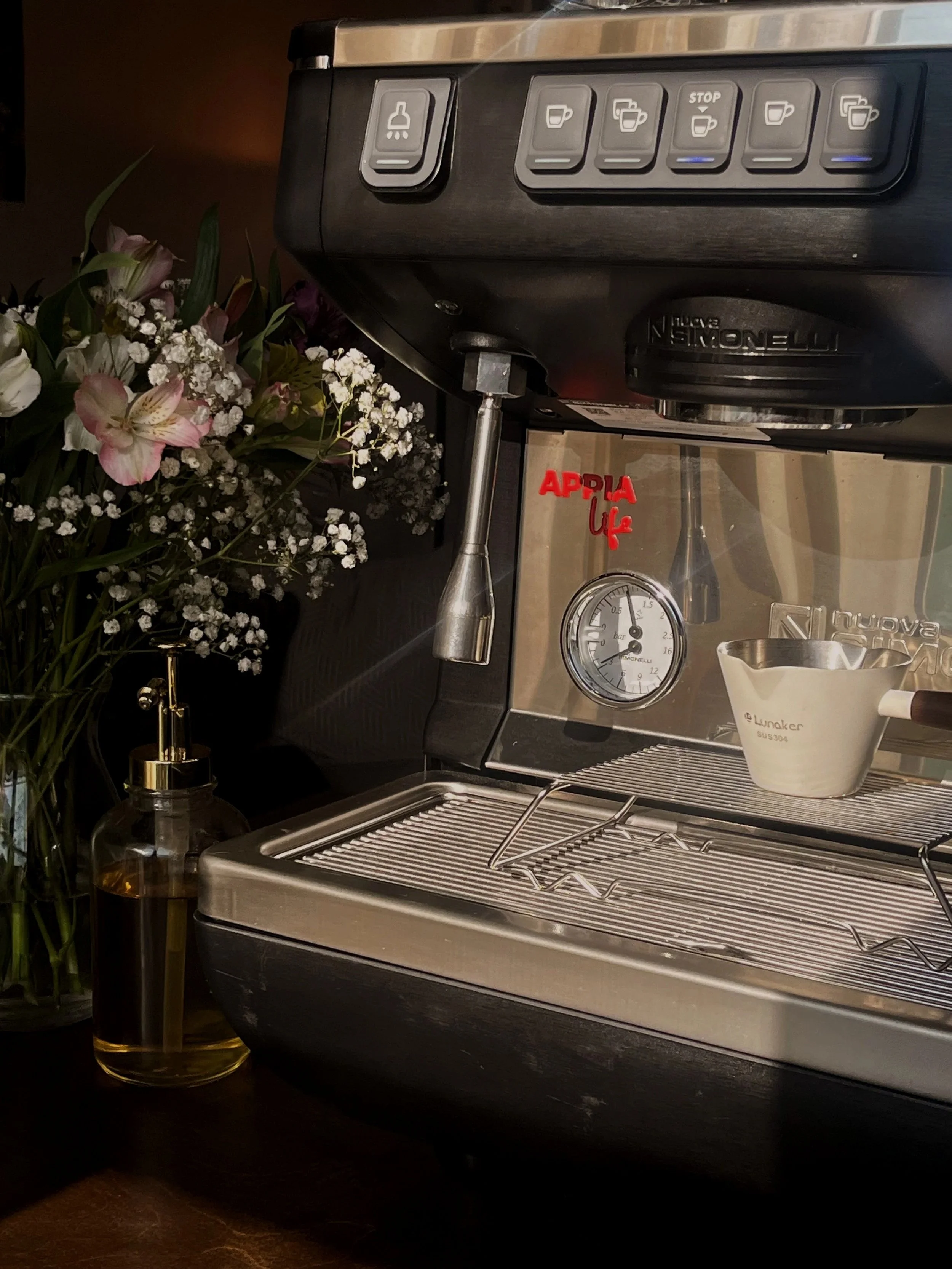 A close-up of a Nuova Simonelli Appia Life espresso machine. The espresso machine has buttons on top and a gauge on the front, as well as an espresso shot glass underneath.
