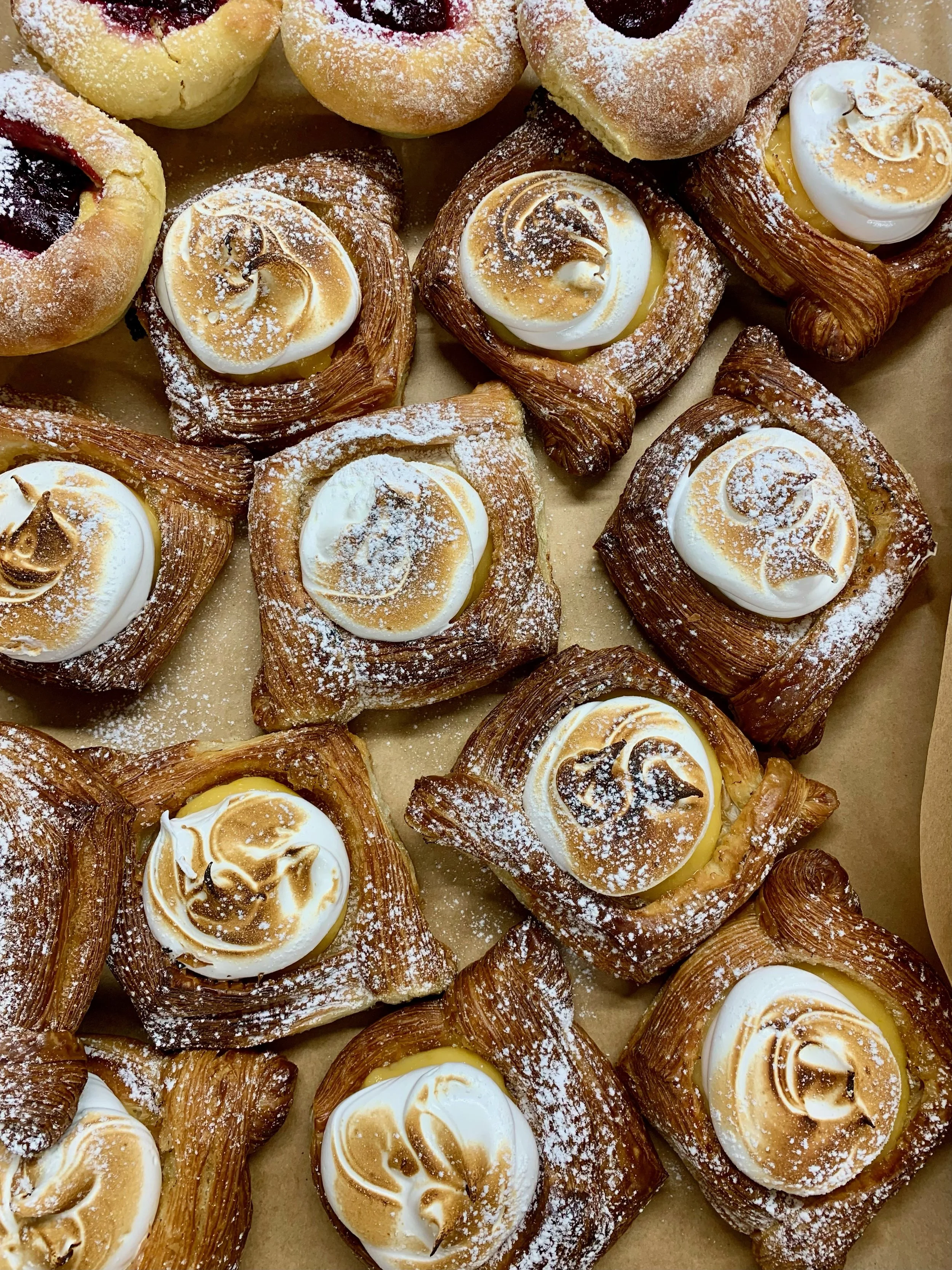 Assorted pastries including Danish pastries topped with meringue, dusted with powdered sugar, on a tray.