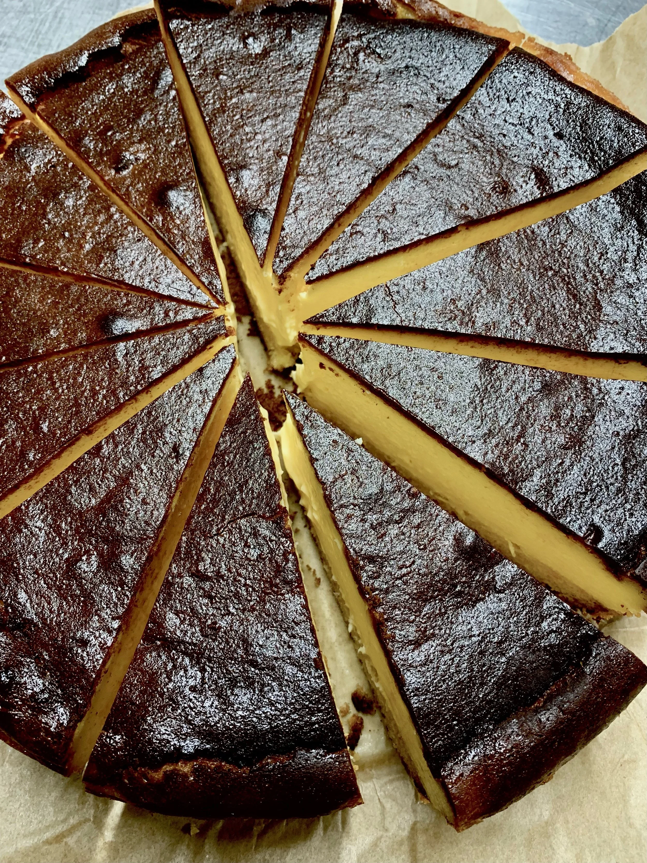 A round cheesecake with a dark brown top, dusted with powdered sugar, sliced into pieces.