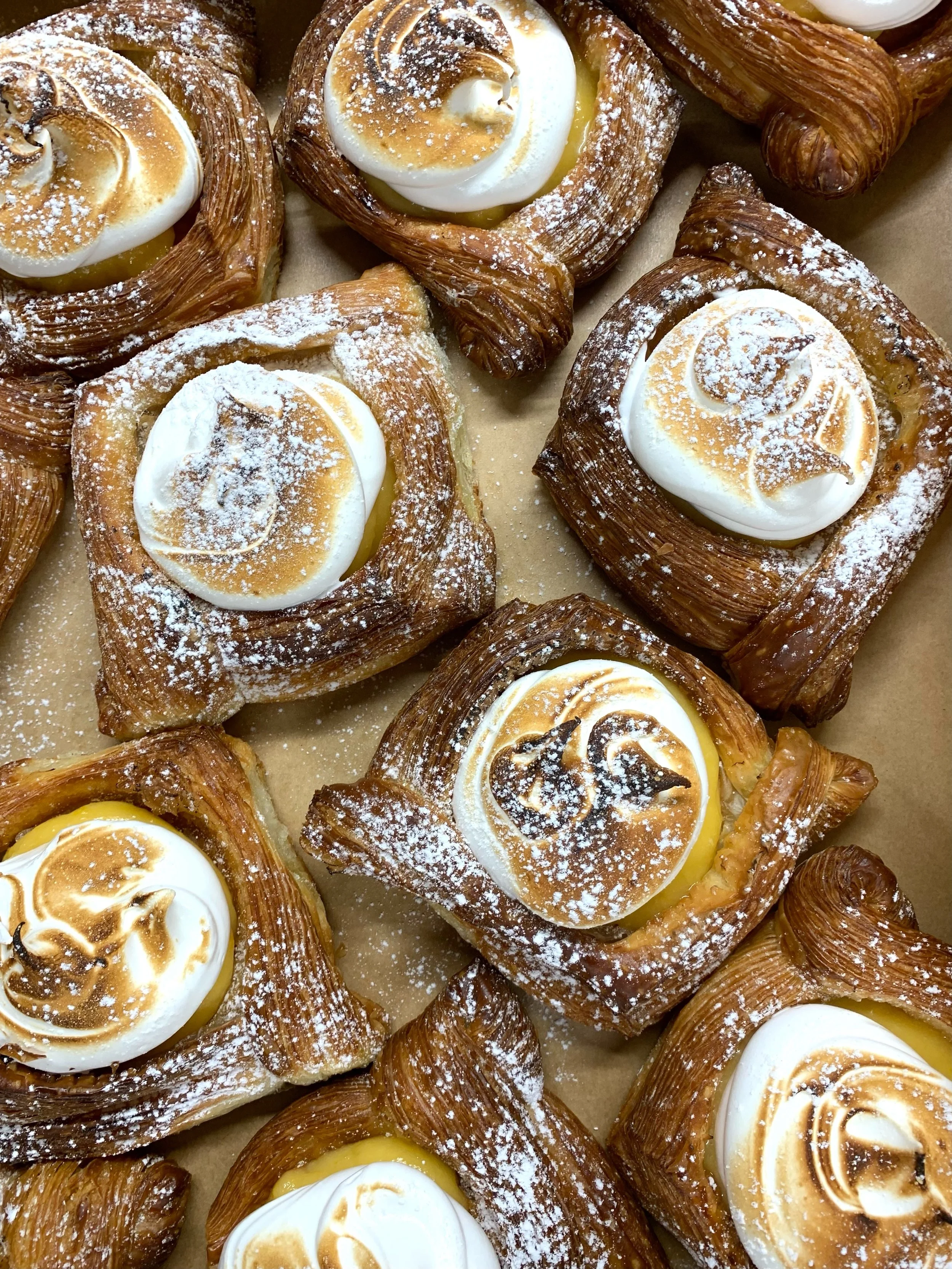 Multiple pastries topped with toasted meringue and dusted with powdered sugar.