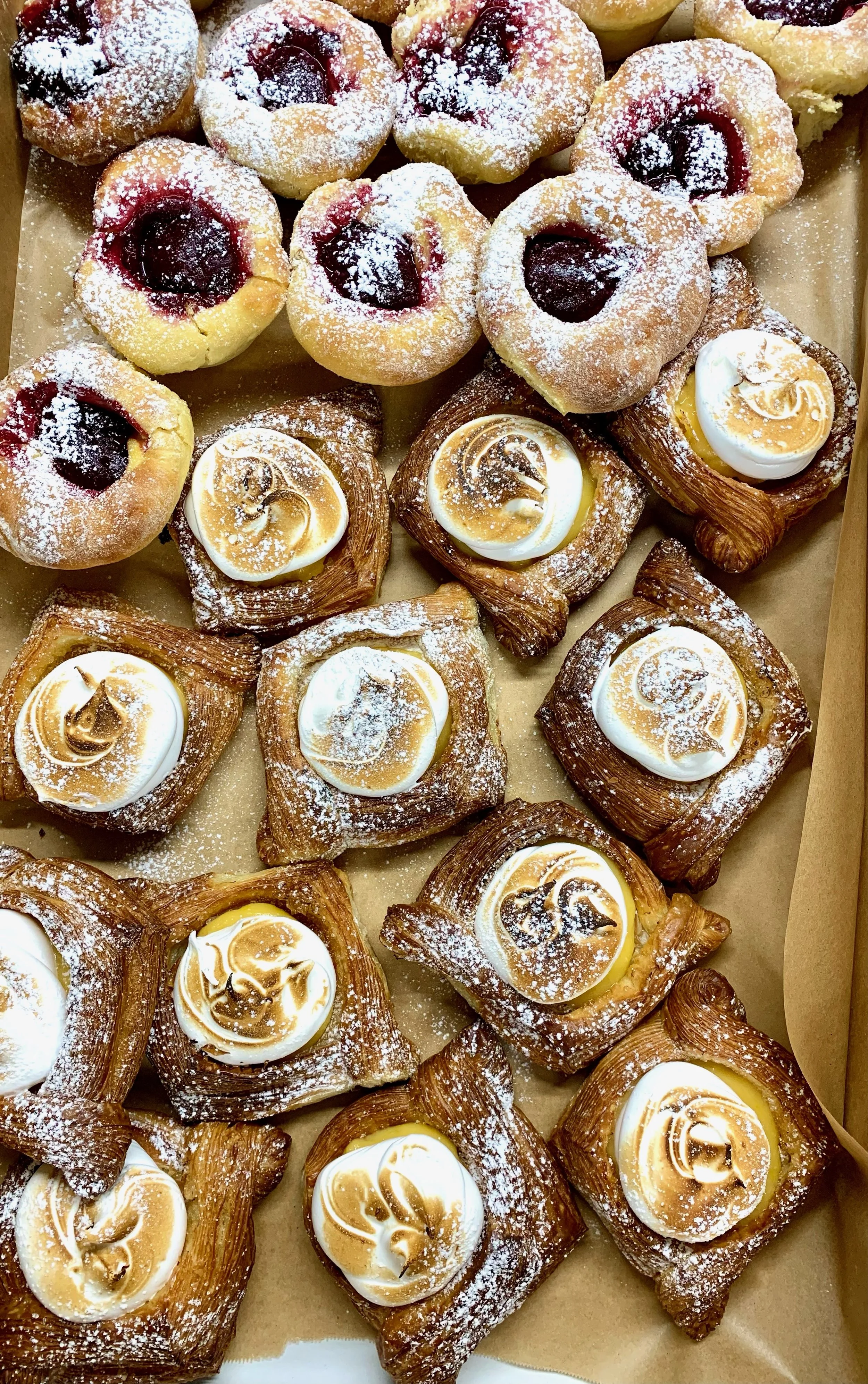 Assorted pastries including Danish pastries with cream and toasted meringue, and fruit-filled pastries dusted with powdered sugar.
