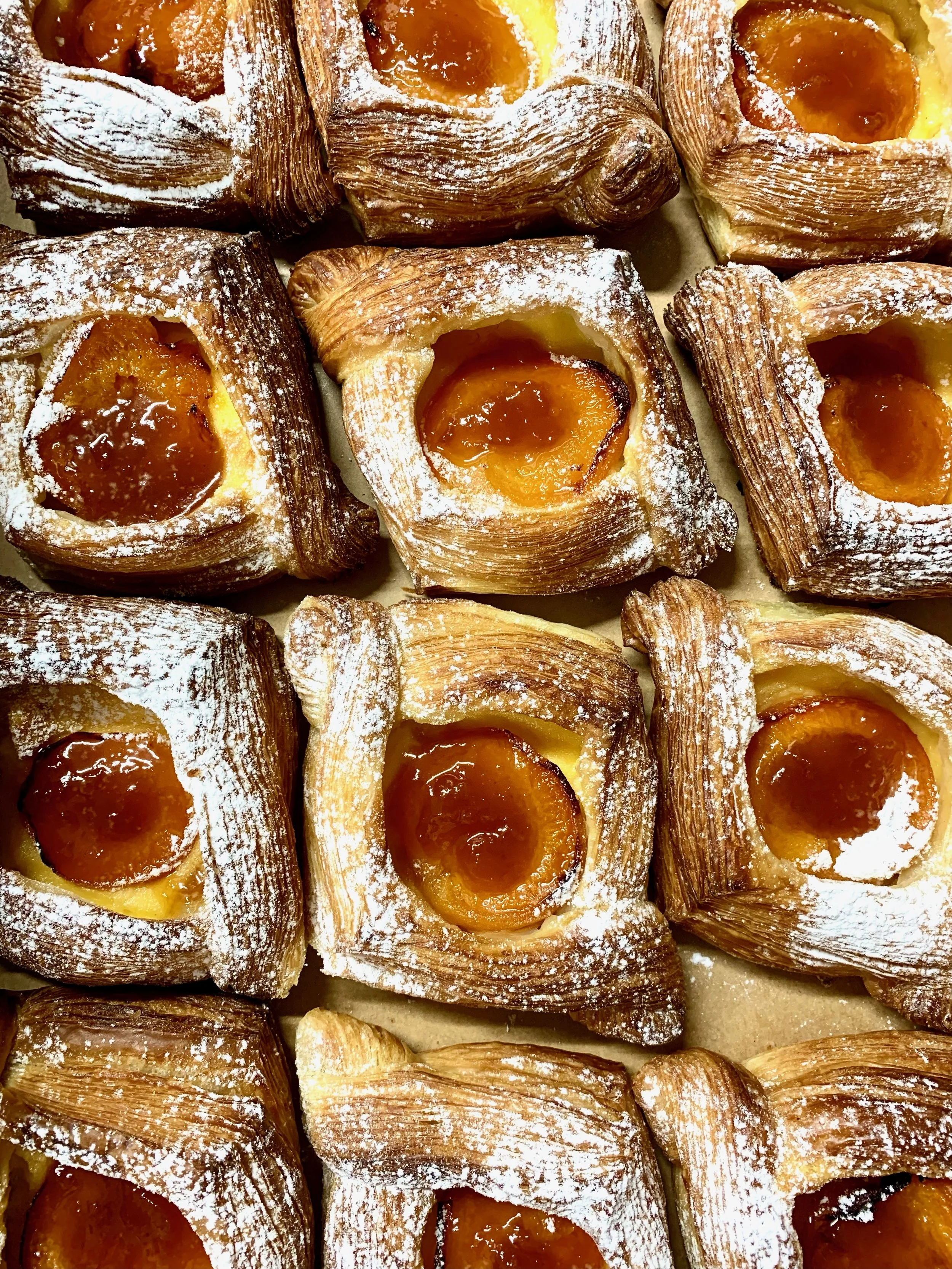 Close-up of multiple Danish pastries topped with powdered sugar, each filled with apricot jam.