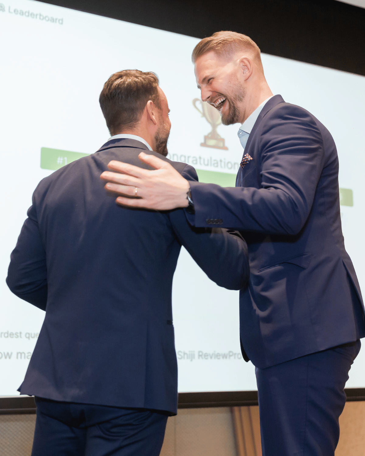 Florian Ultsch and an Southeast Asian business parnter in suits sharing a joyful moment on stage during an event in Thailand.