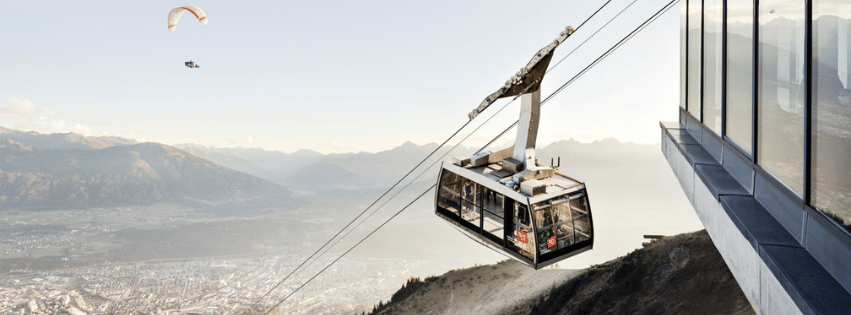 Innsbrucker Nordkettenbahnen with a paraglider flying and a Austrian mountain range in the background.