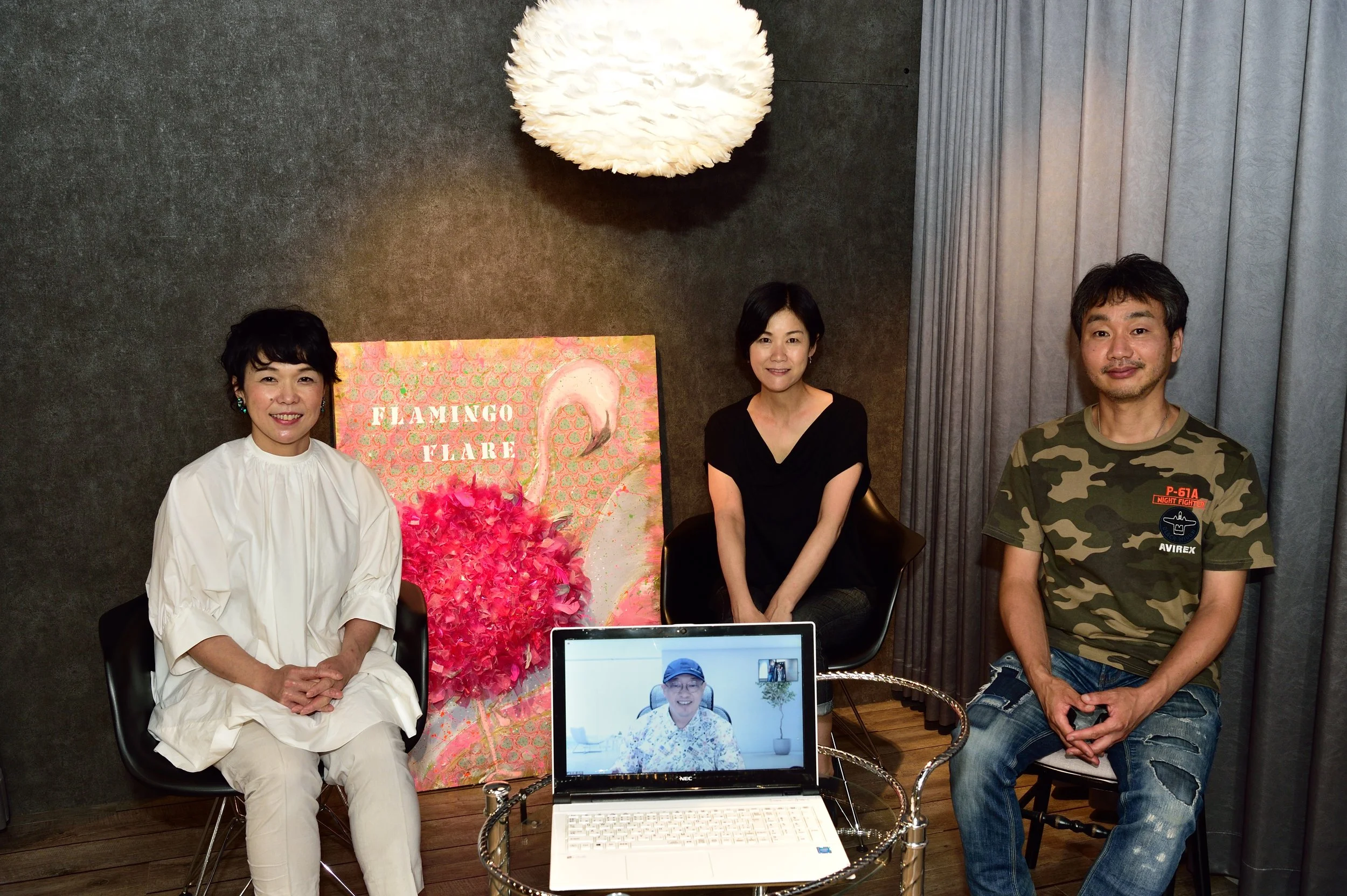 室内の会議室で4人の人が座っている写真。背景には「FLAMINGO FLARE」という看板とピンク色のフラミンゴの装飾が見える。