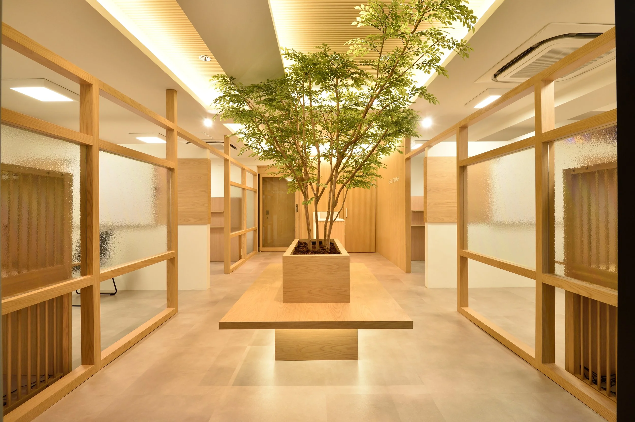 室内に観葉植物が置かれた空間。木製の仕切りとテーブルが配置されたシンプルなデザインの空間。