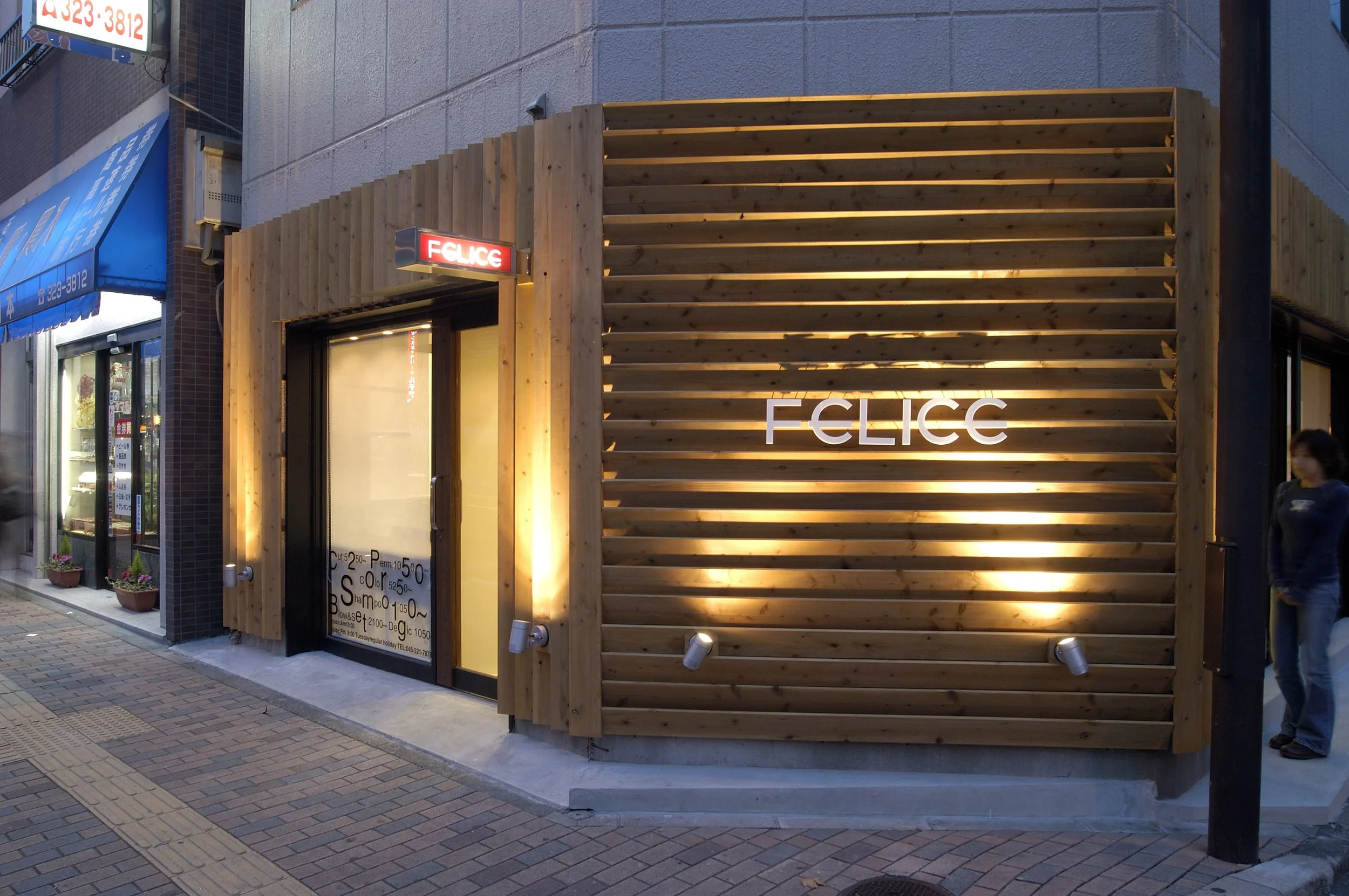 木製の外観を持つ店の入り口。店名は「FELICE」と書かれ、照明が灯っている。周囲にはガラスのショーウィンドウや店の看板、歩道があります。