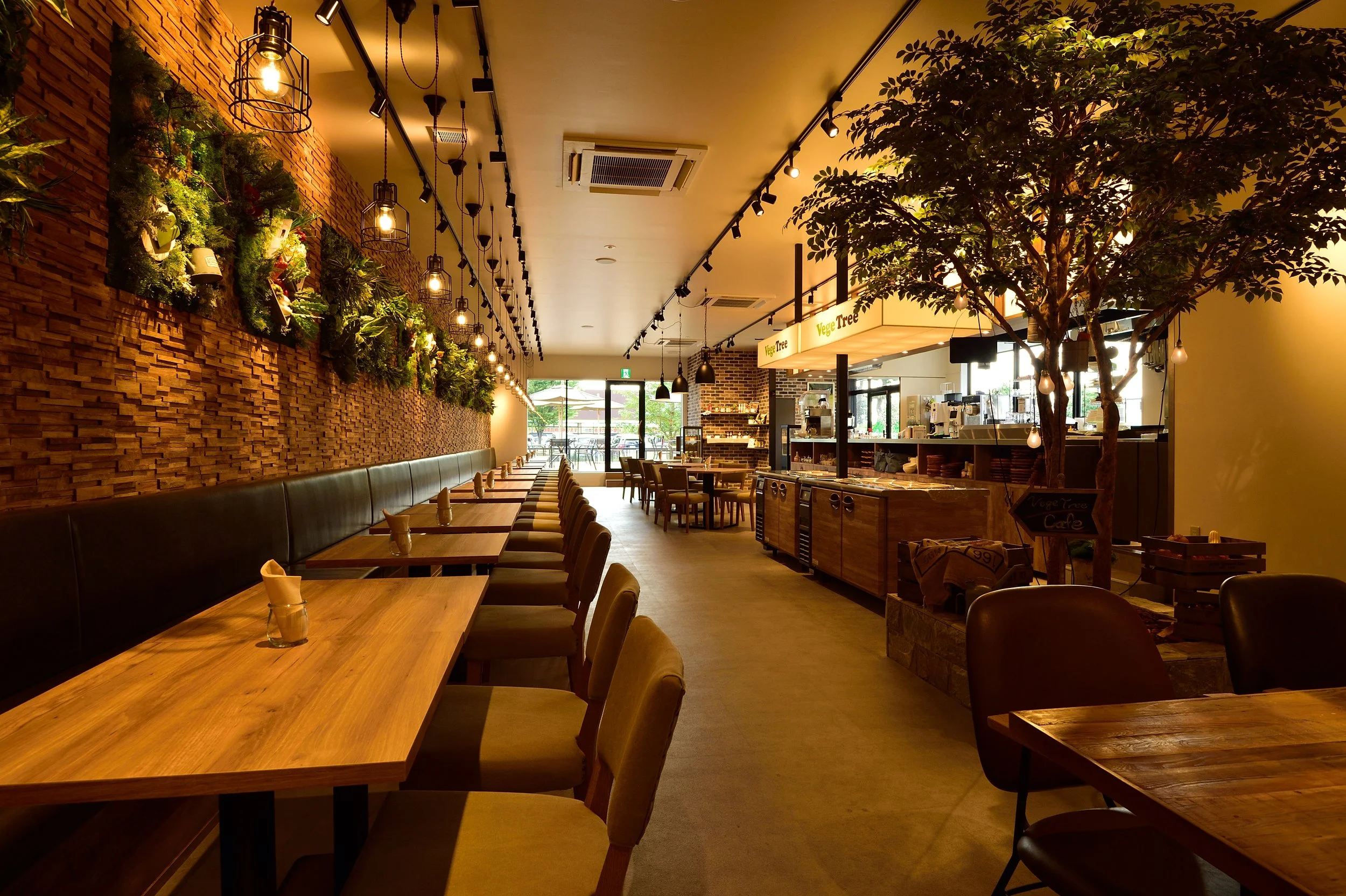 木のテーブルと椅子が並ぶ、壁に緑の植物が飾られた落ち着いたカフェの interior.