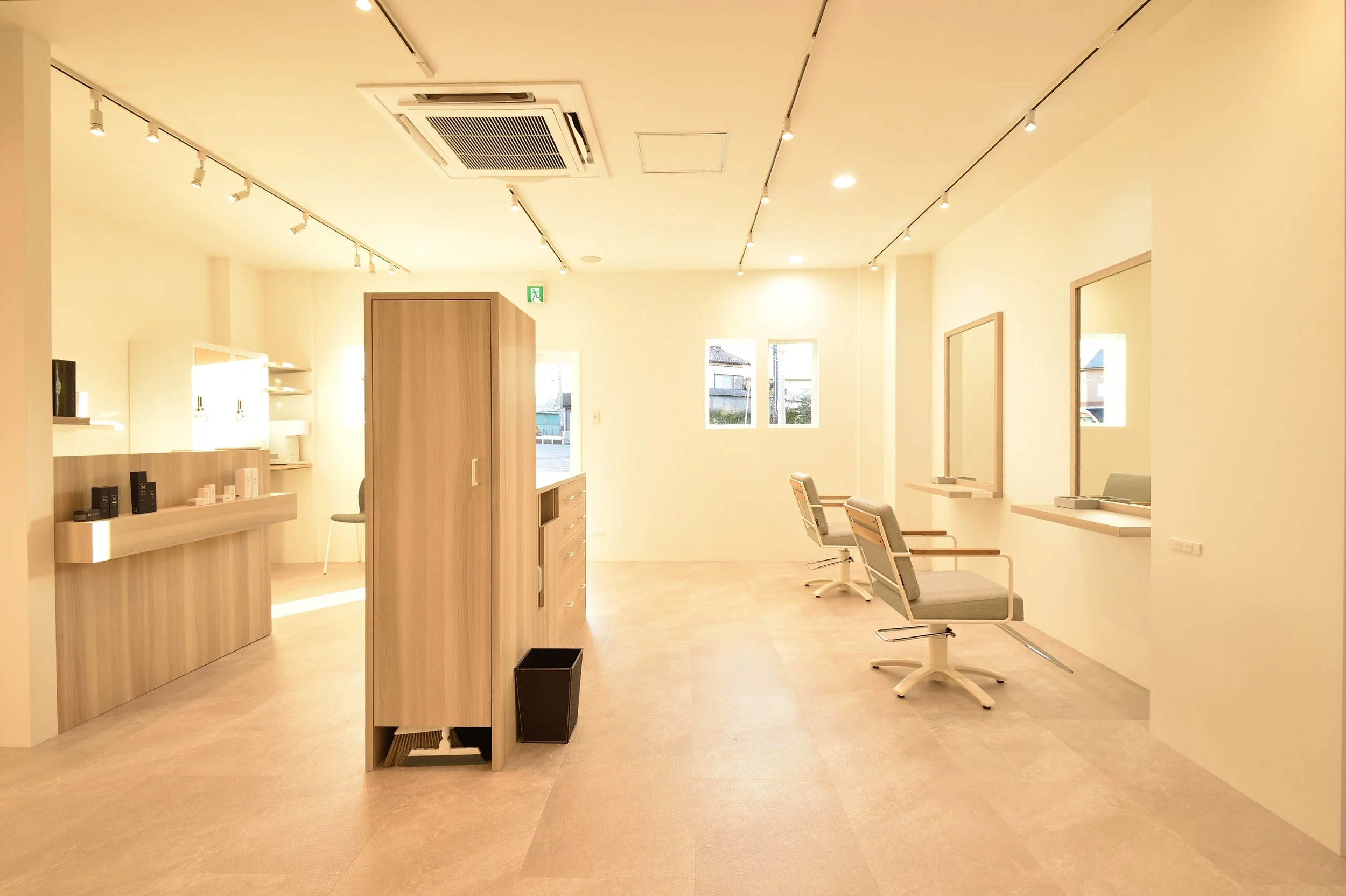 明るい照明の美容院の interior with スタイリストの机、鏡、椅子があります。