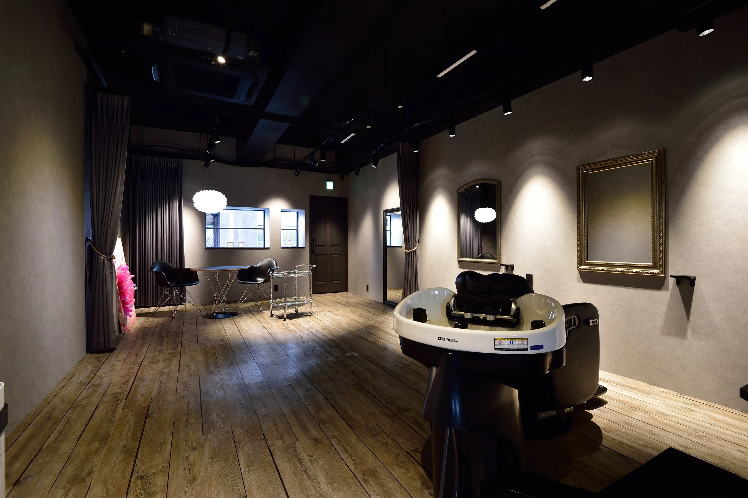 木製の床と壁紙のある部屋で、丸い鏡とソファー、ローテーブル、赤い羽毛の飾りとベビーバスが置かれた部屋の写真。暗めの照明で落ち着いた雰囲気。