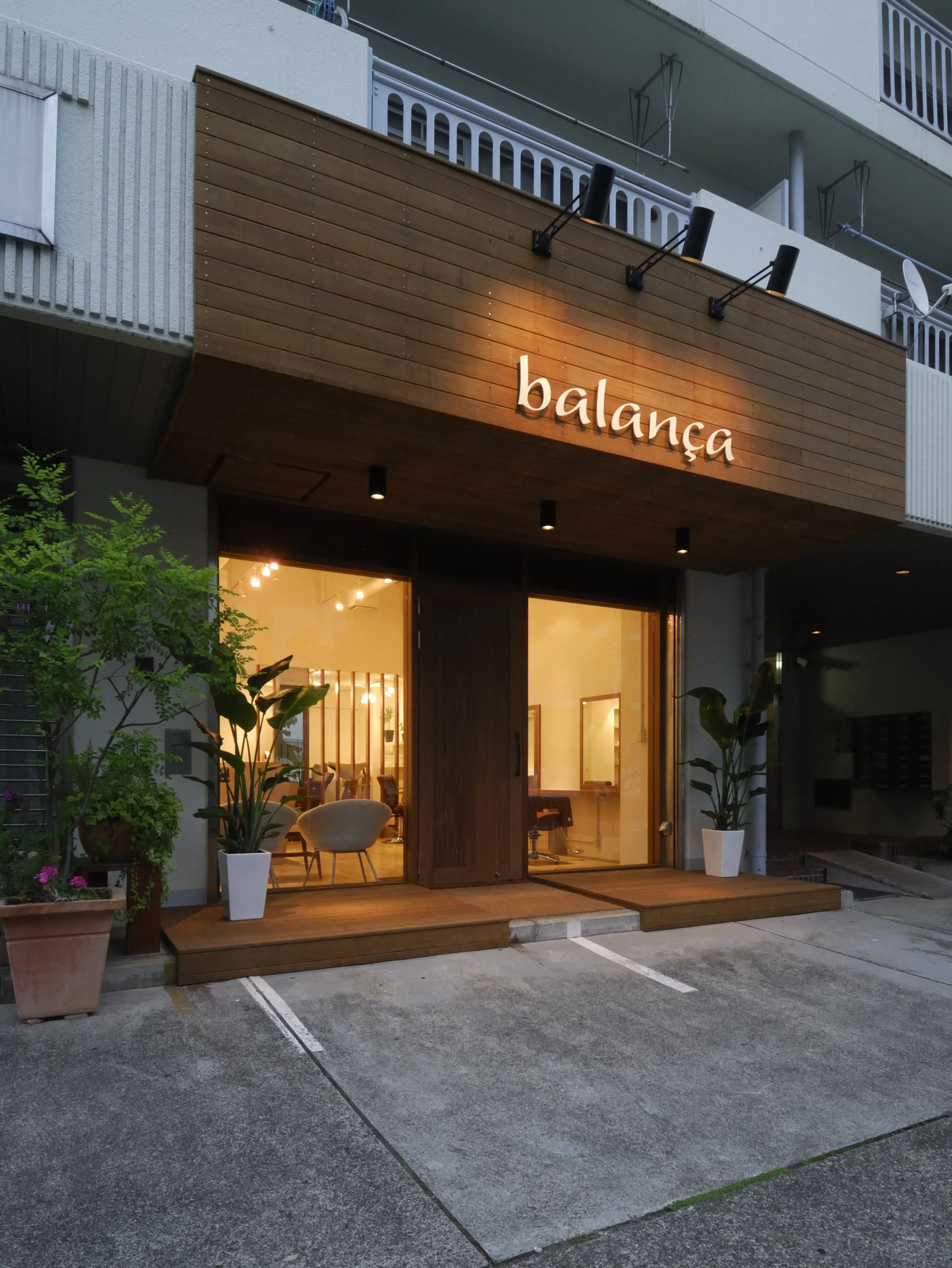 夜のレストラン「balança」の外観。木製の看板と大きな窓から中の照明が見える。植物が置かれ、駐車場が空いている。