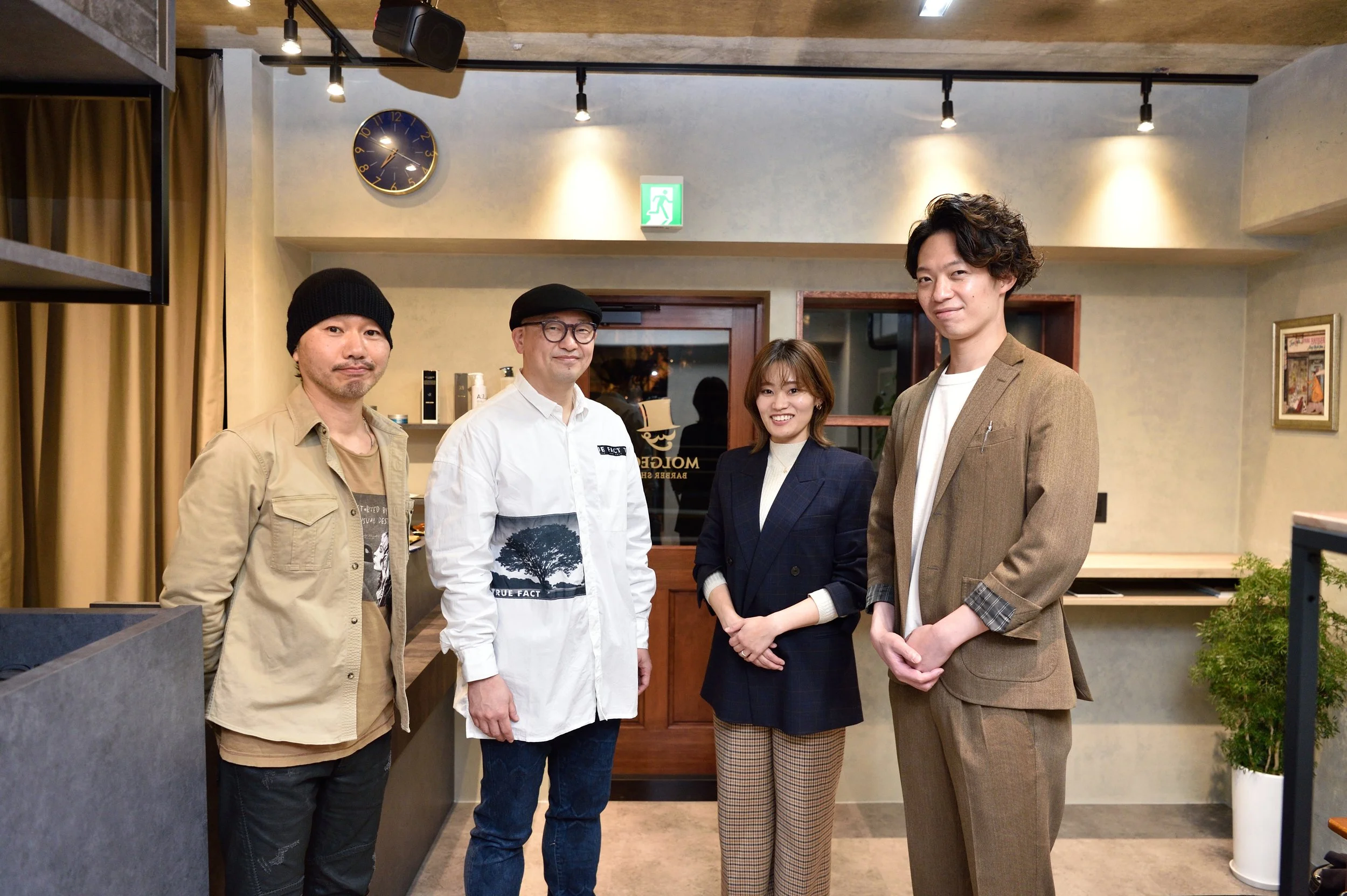 レストランのスタッフとお客様が笑顔で写真を撮っている。背景には時計と緑の避難経路標識が見える。