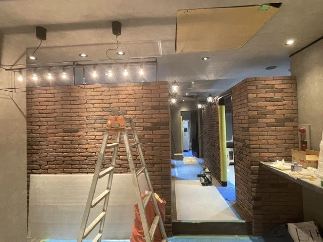 内装工事中の建築現場の一角。レンガ壁と天井の一部に照明や工事用道具が見える。