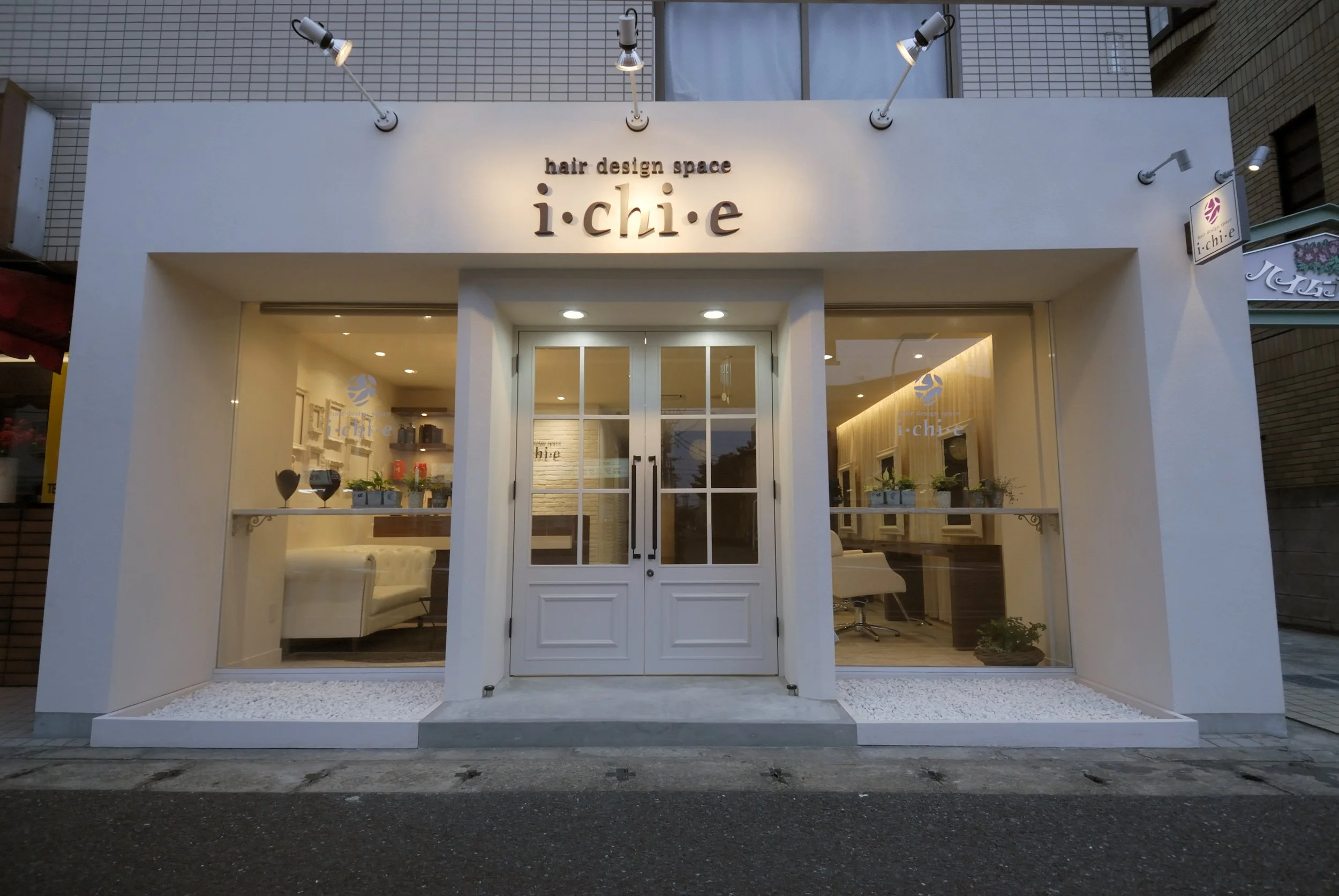 白い外観のヘアサロン店の正面。入り口にはガラスドアと大きな窓があり、店内の一部が見える。看板には「hair design space i·chi·e」と記されている。