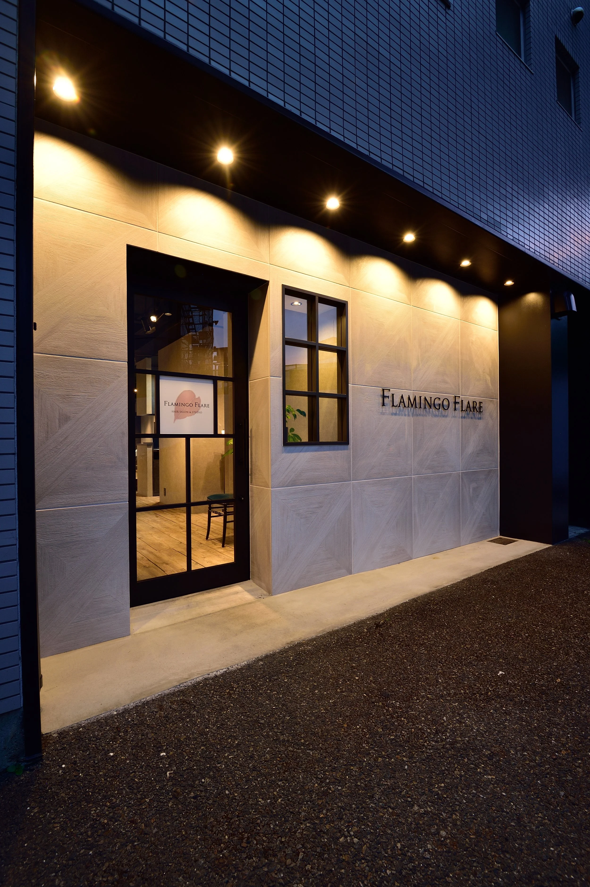 夜景の中にある建物の入口。看板には「FLAMINGO FLARE」と書かれている。外壁はレンガ調で、暖色系の照明が天井の下に設置されている。