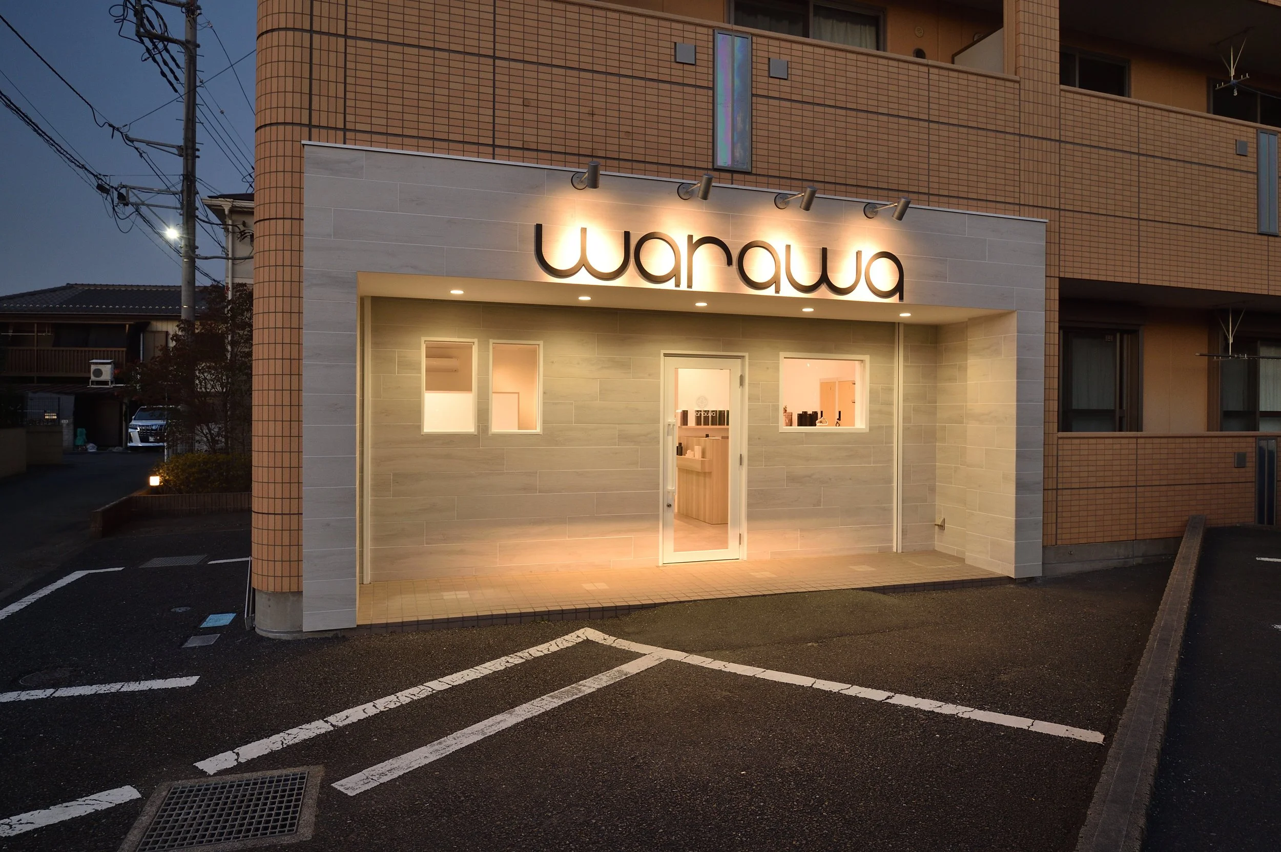 夜に点灯している店の看板に「warawa」と書かれている建物の外観。駐車場が写っている。