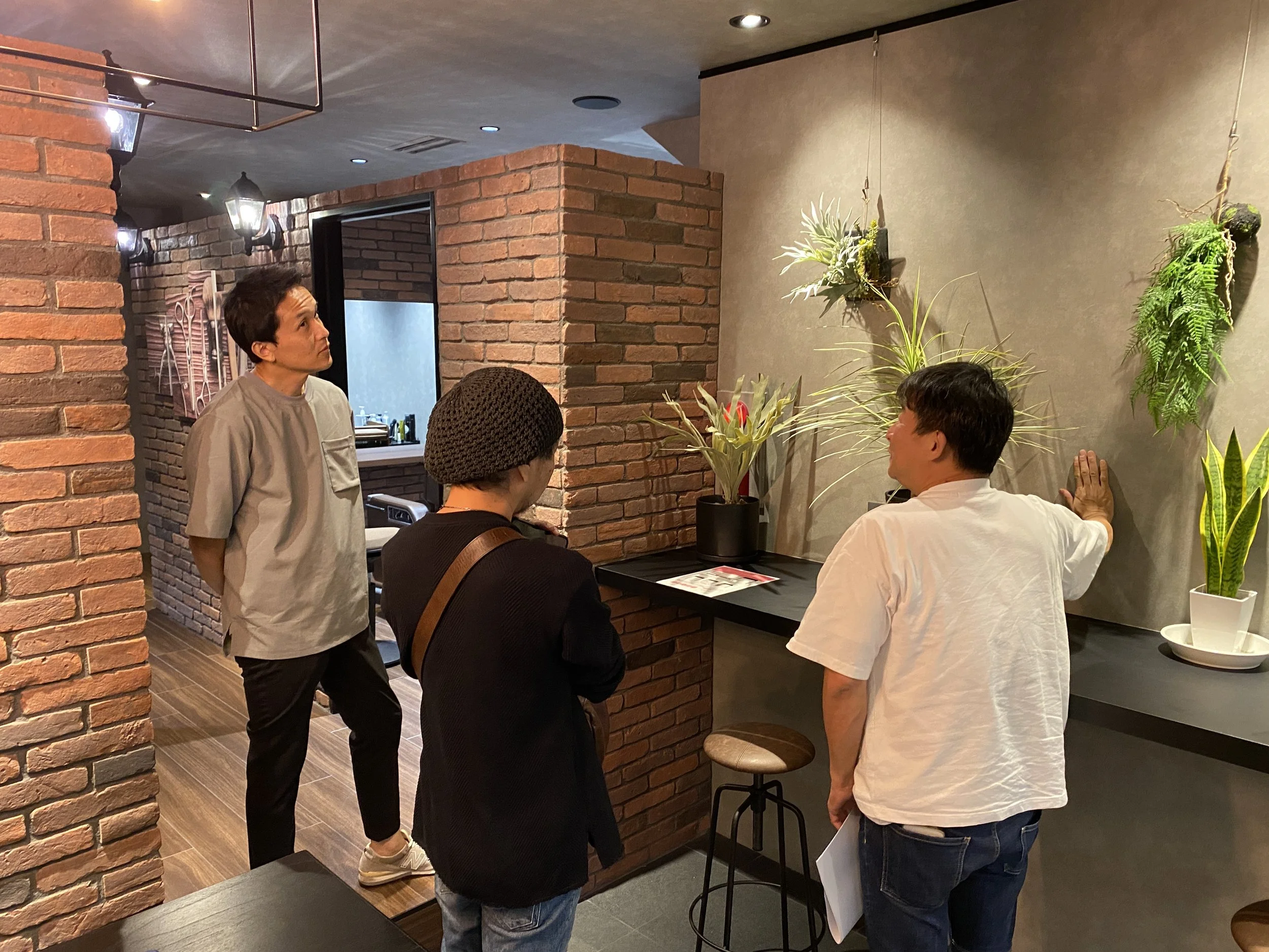 レストランの中で、男女数人が会話をしている様子。背景はレンガ壁と観葉植物が飾られている。