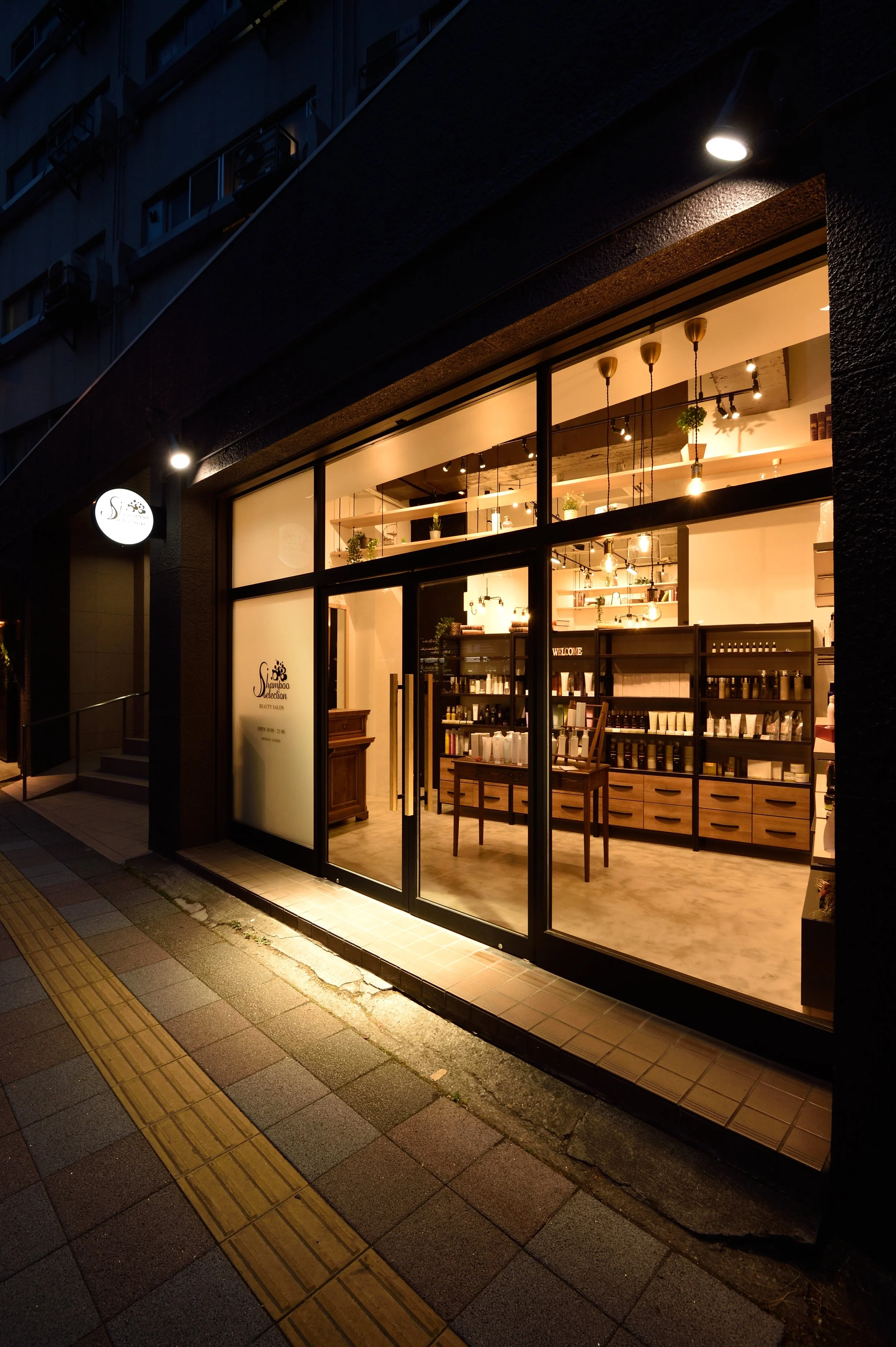 夜の美容院の店内、暖かい照明と棚に並ぶヘア用品が見える。