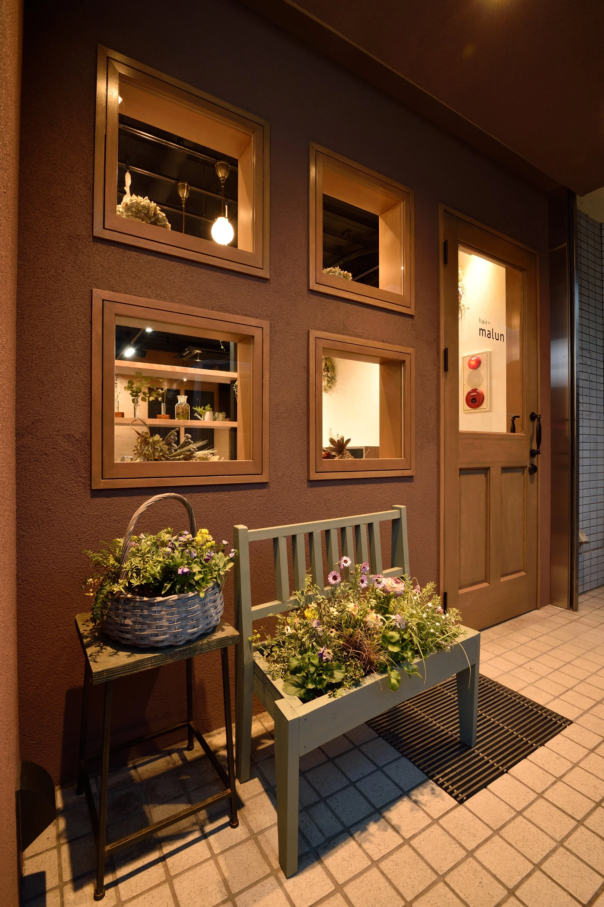 夜の店の入り口に花の置物や観葉植物が飾られた壁とドアが映っている。