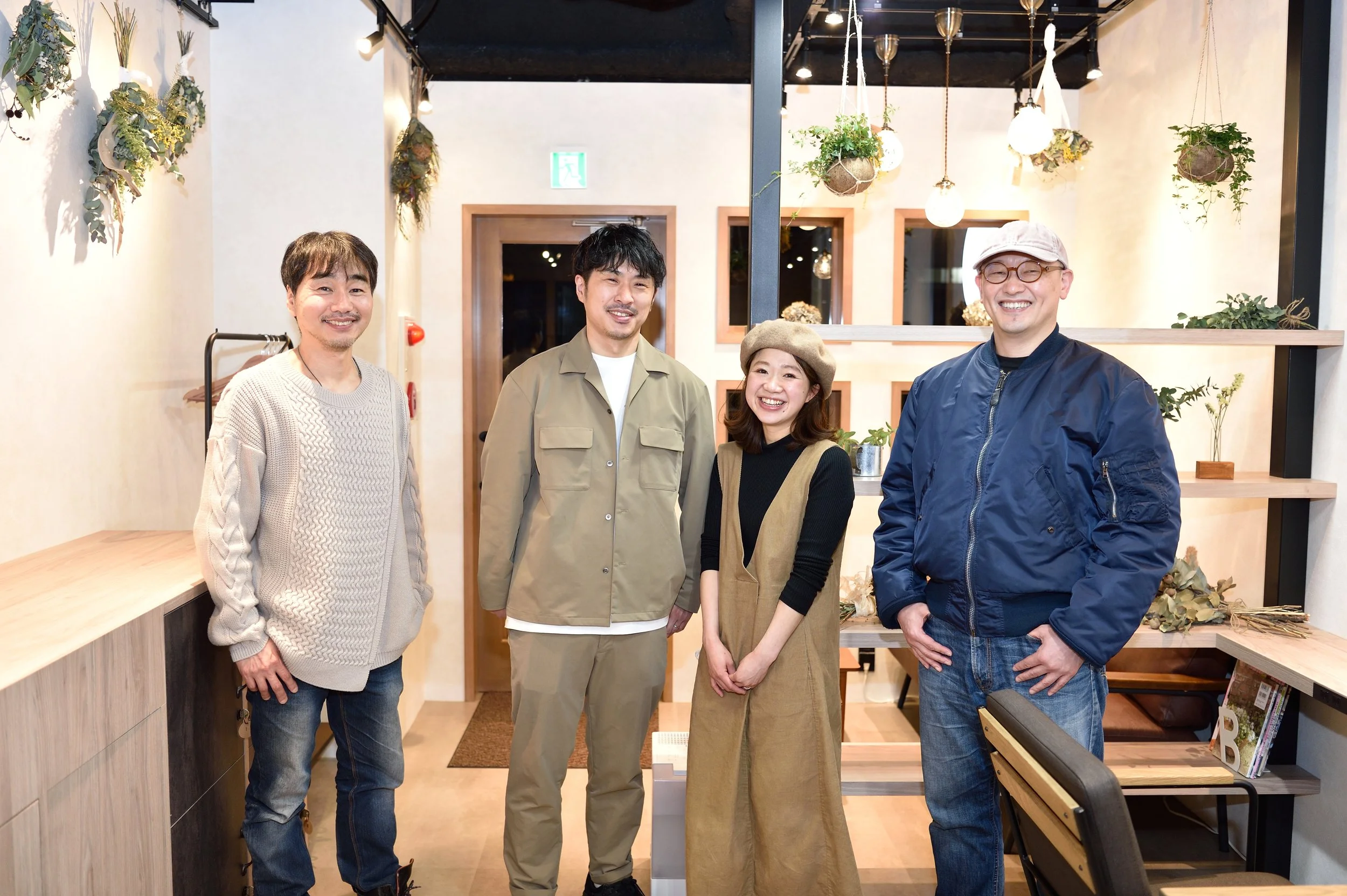 笑顔の男女四人が室内でポーズをとっている。背景には植物と照明が飾られている。