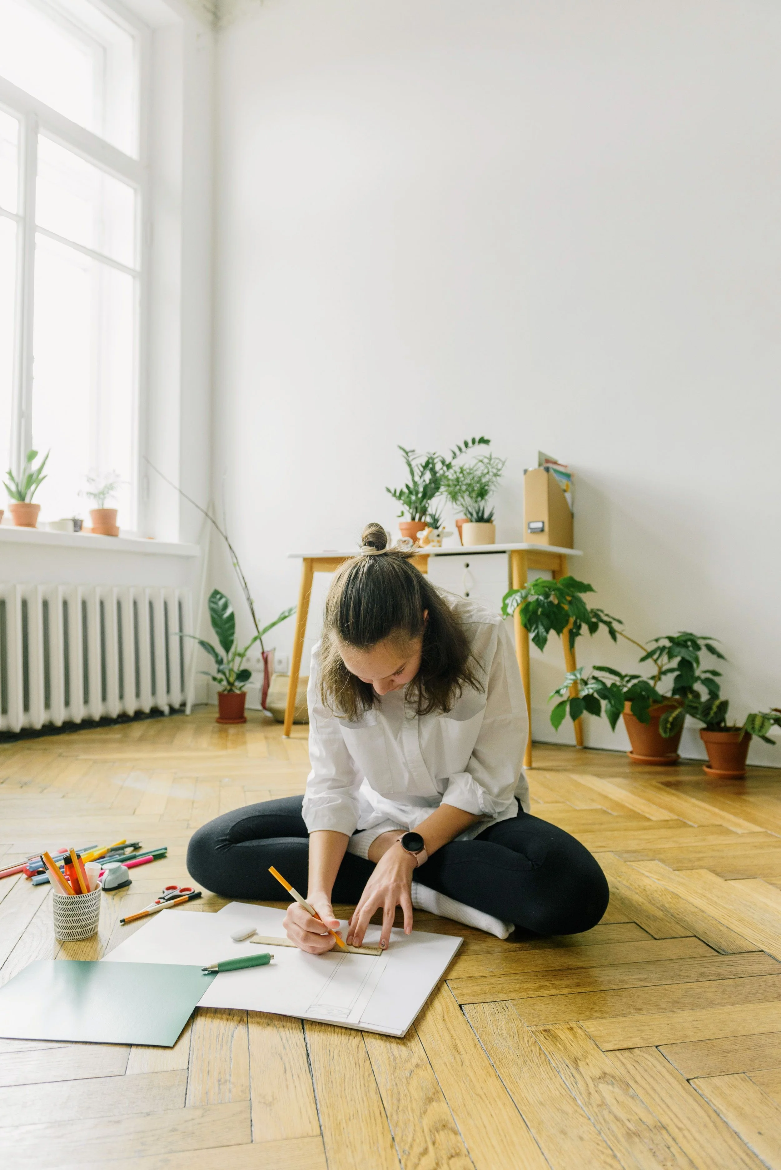 Woman sitting on the floor drawing in a notebook surrounded by art supplies, unable to stop and rest — anxiety therapy in Charlottesville, Virginia.