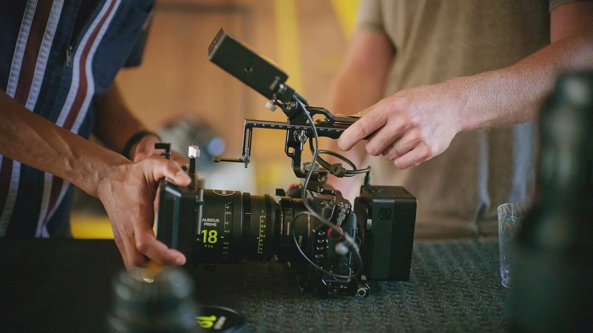 A person helping install a camera lens on a cinema camera. The camera is rigged with a monitor and top grip handle.