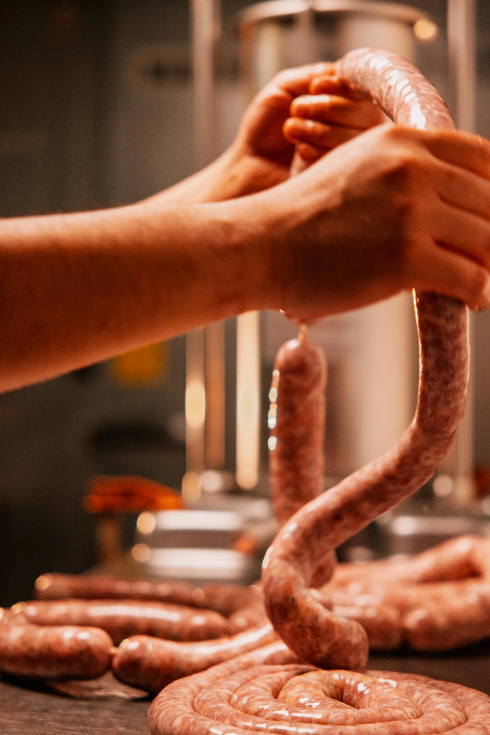 Person handling raw sausages in a sausages manufacturing or preparation setting.