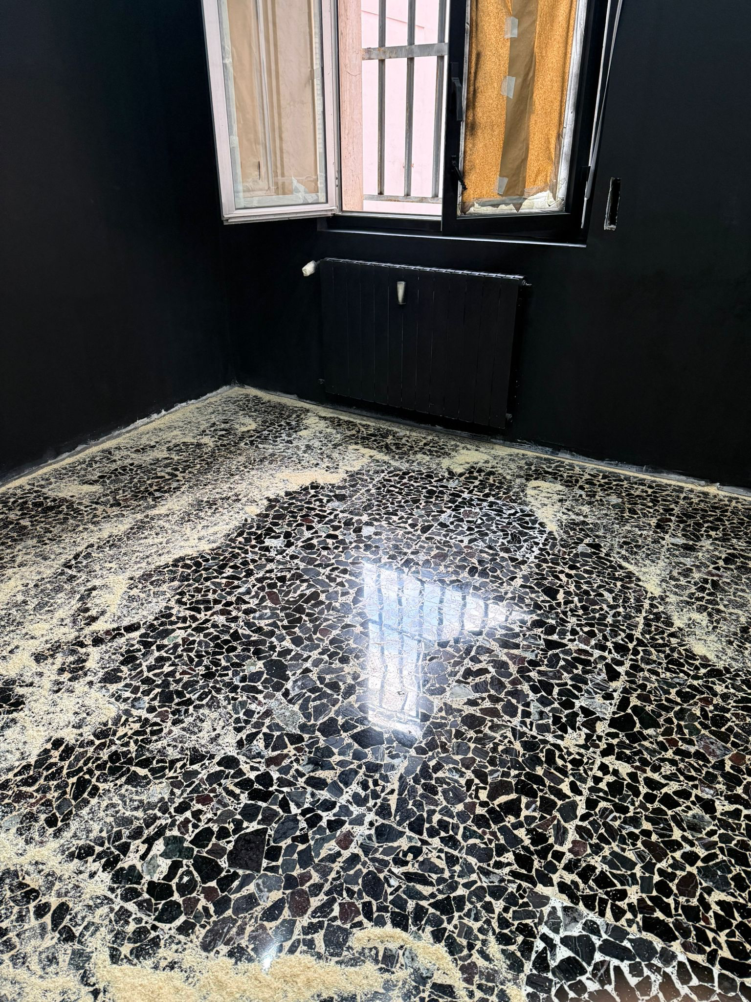 Empty room with black painted walls, open window, black radiator, and black and beige mosaic tile floor.