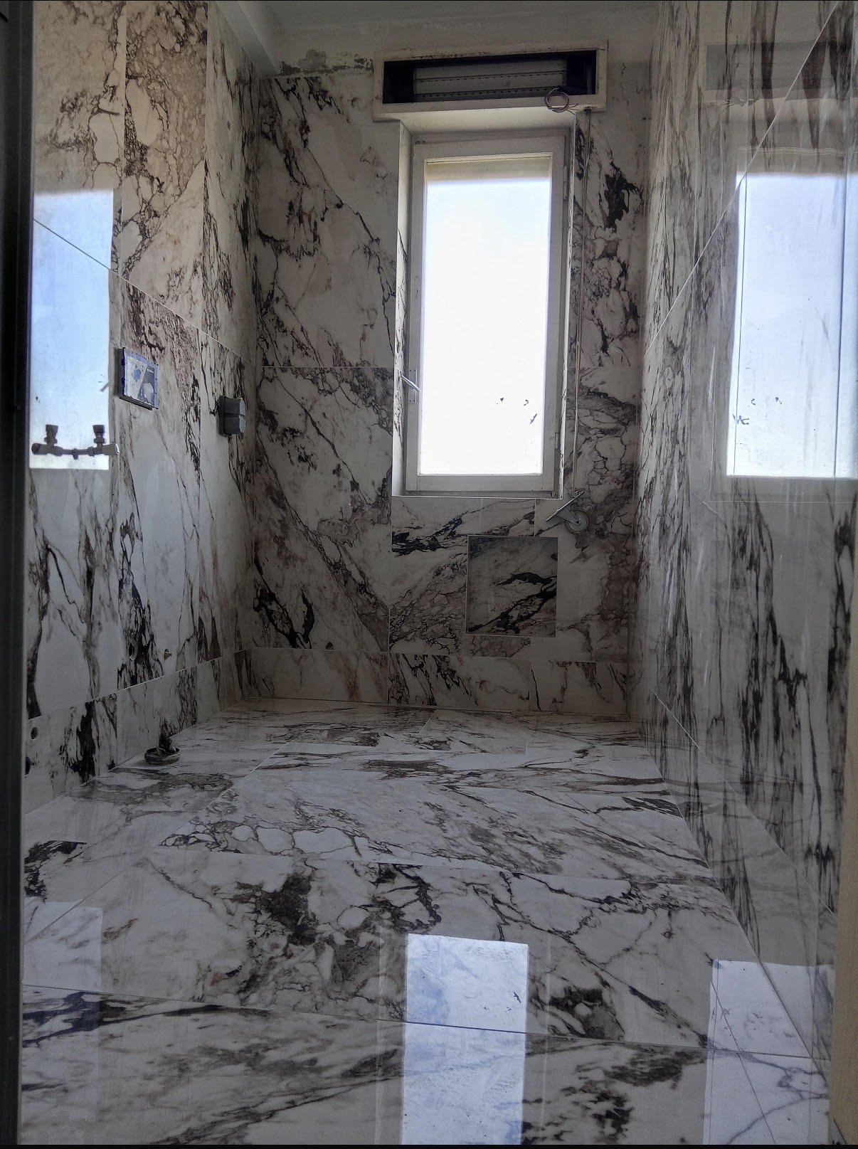 Empty bathroom with marble walls and floor, a window, and construction elements visible.