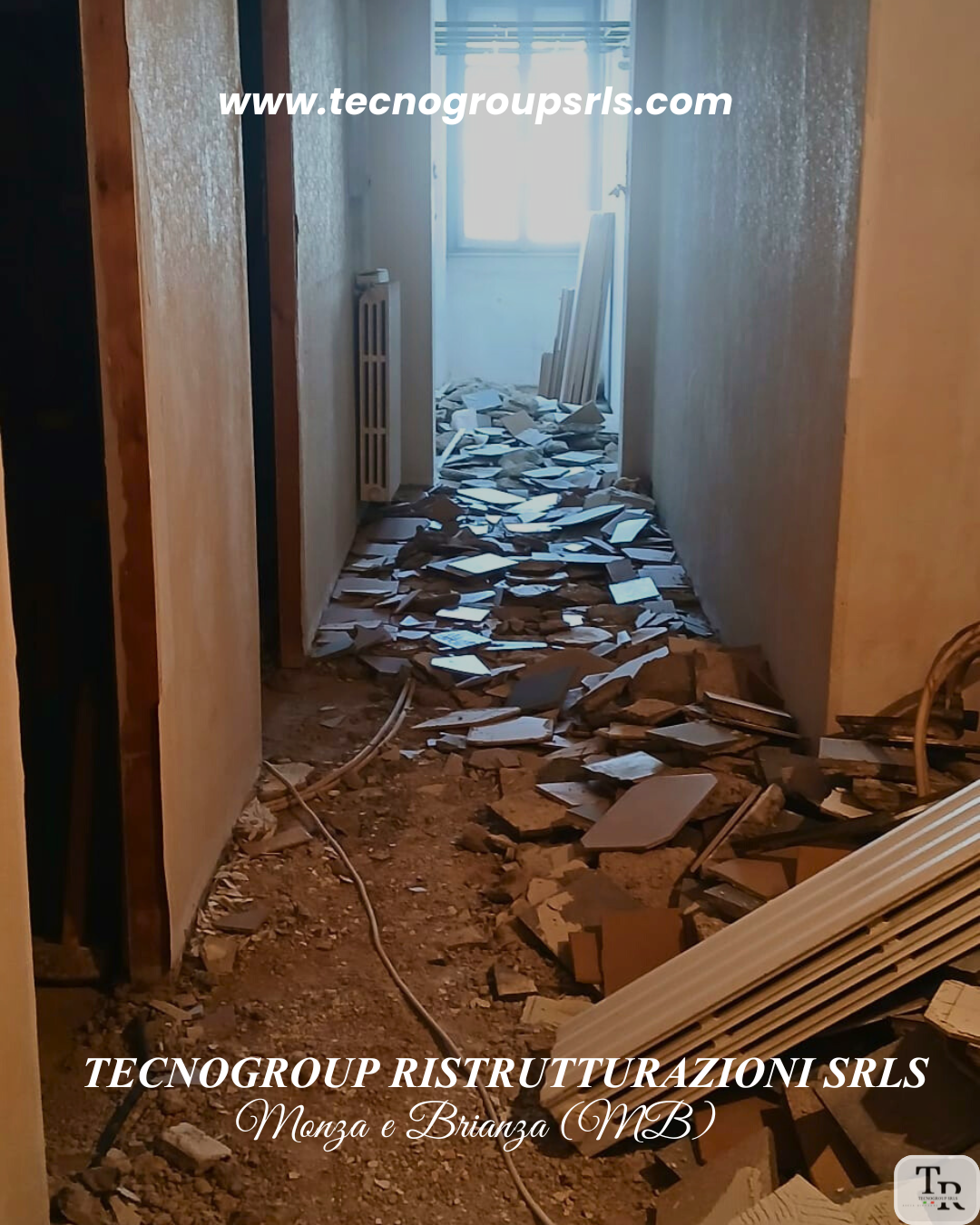 Construction debris in a narrow hallway with a pile of broken tiles and materials on the floor, and a window at the end of the corridor.