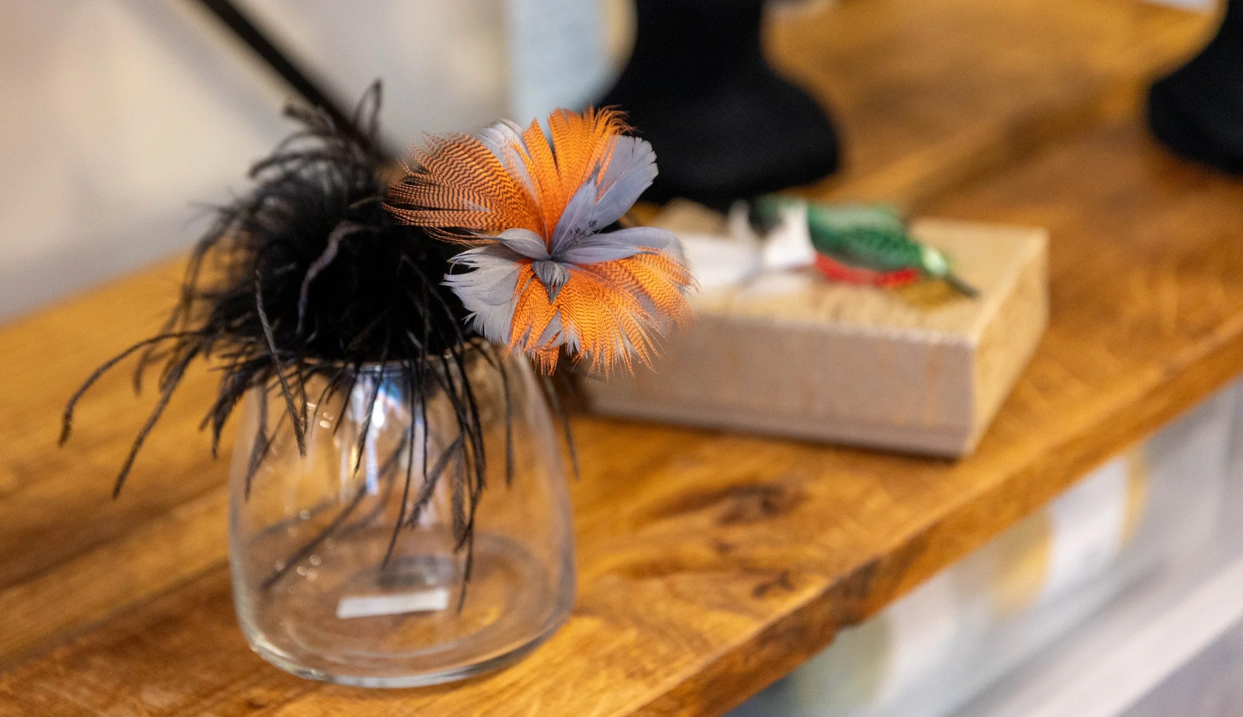 Vase en verre contenant des montages de plumes colorées, pour accessoires de tête.