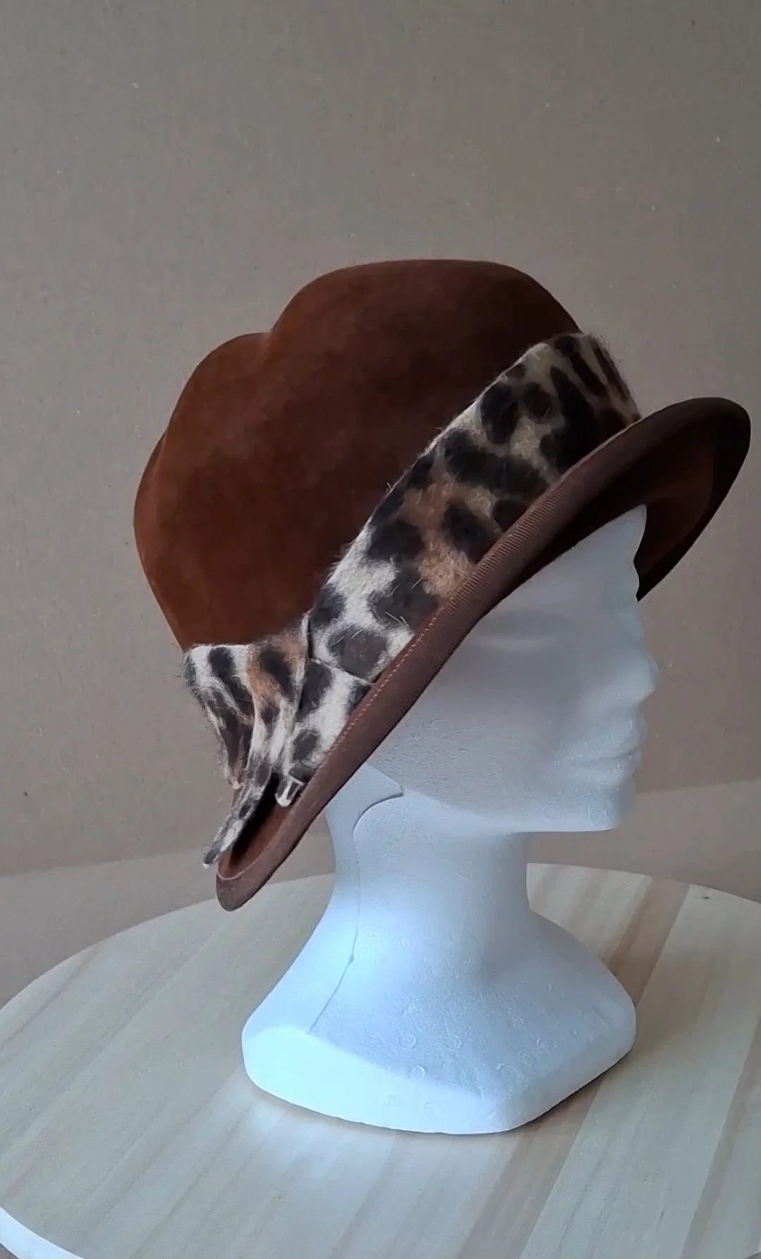 Un chapeau à large bord avec un motif de léopard, posé sur une tête en polystyrène dans une pièce intérieure.
