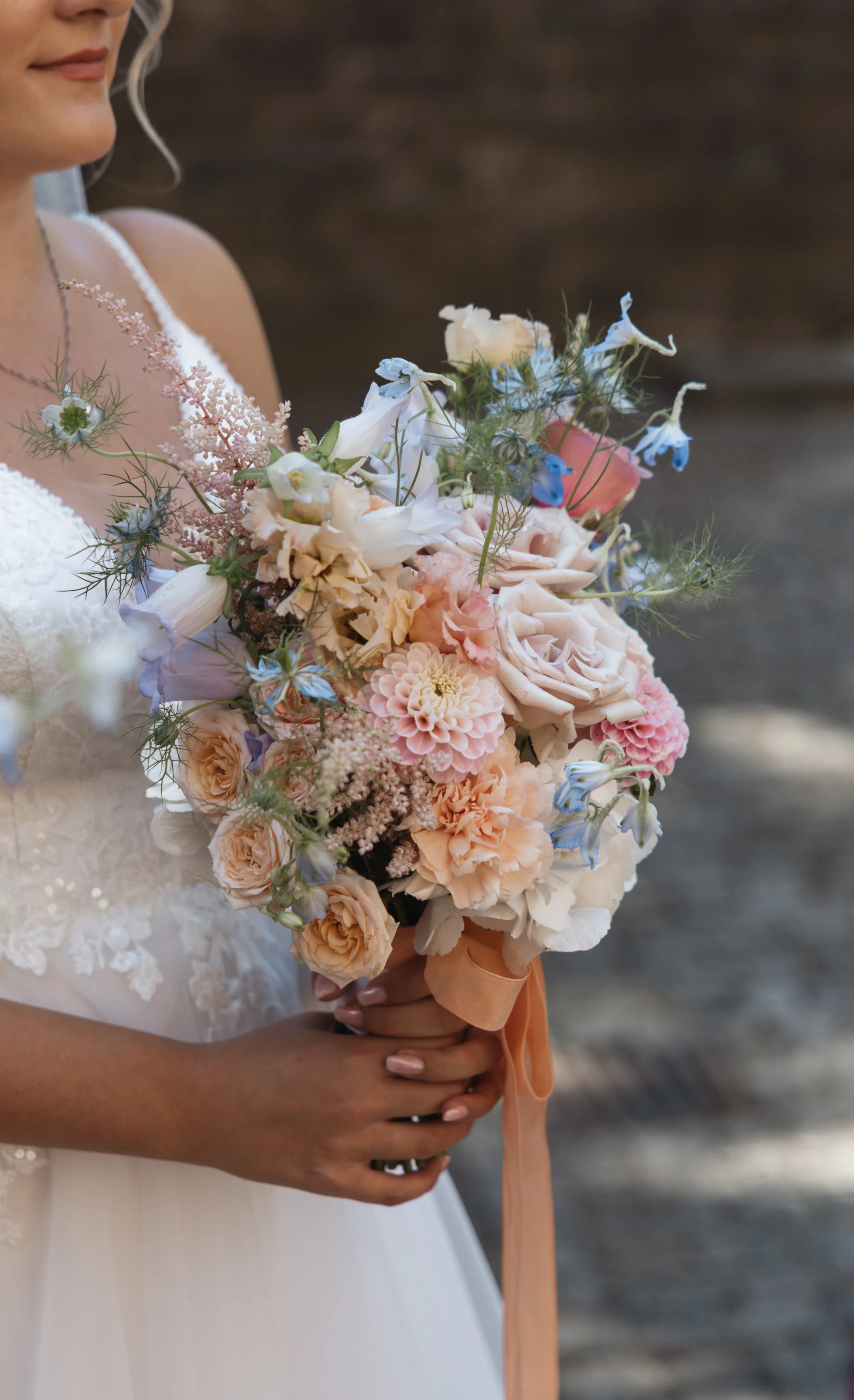 Braut in weißem Kleid hält einen großen Blumenstrauß mit Pfingstrosen, Rosen und anderen Blumen in Pastellfarben.