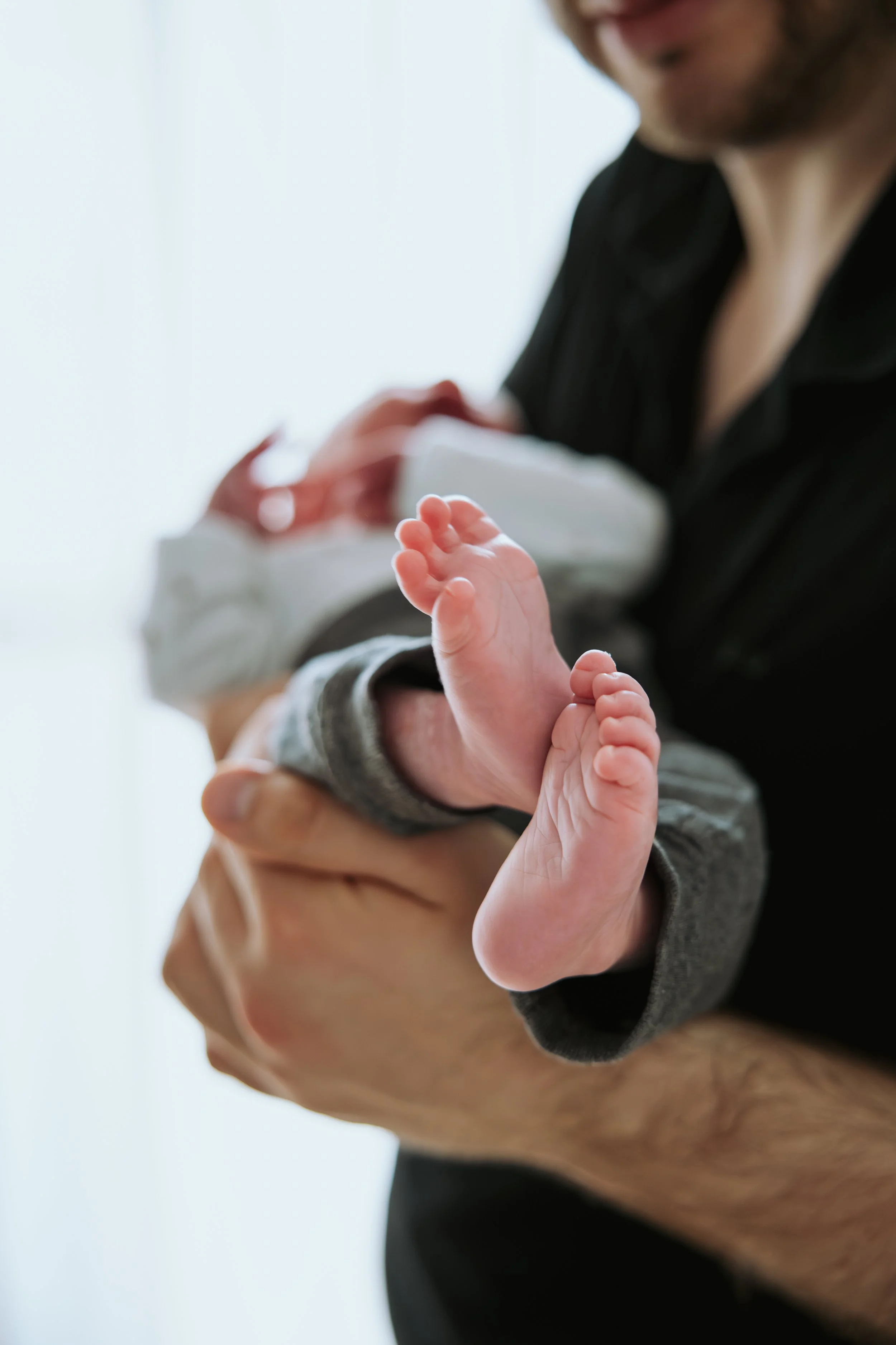 Nahaufnahme, wie ein Mann ein Baby im Arm hält. Fokus sind die kleinen Baby Füße.