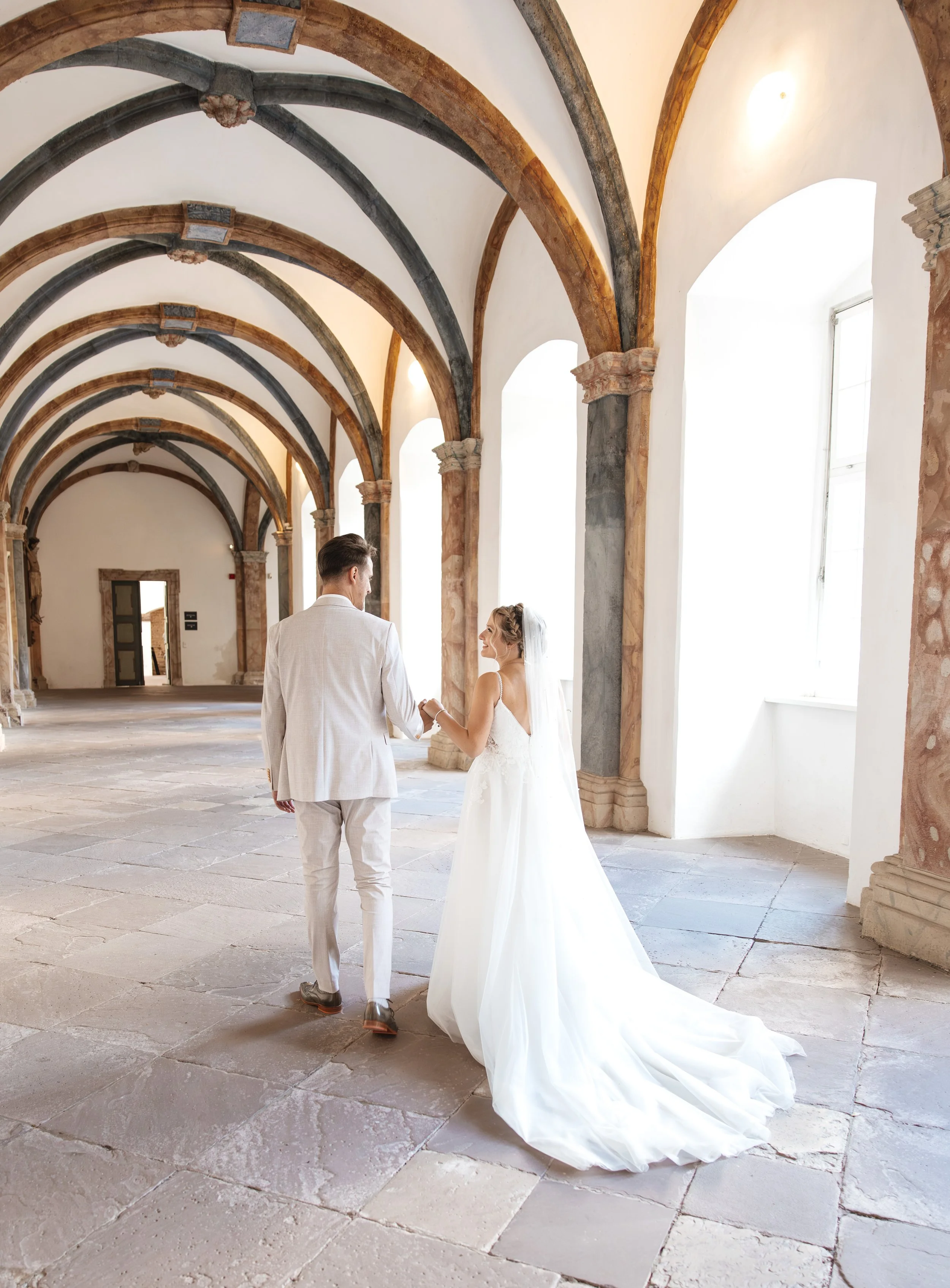 Ein Brautpaar bei einer Hochzeit in einem alten Gebäude mit hohen, gewölbten Decken und großen Fenstern, die viel Licht ins Innere lassen.