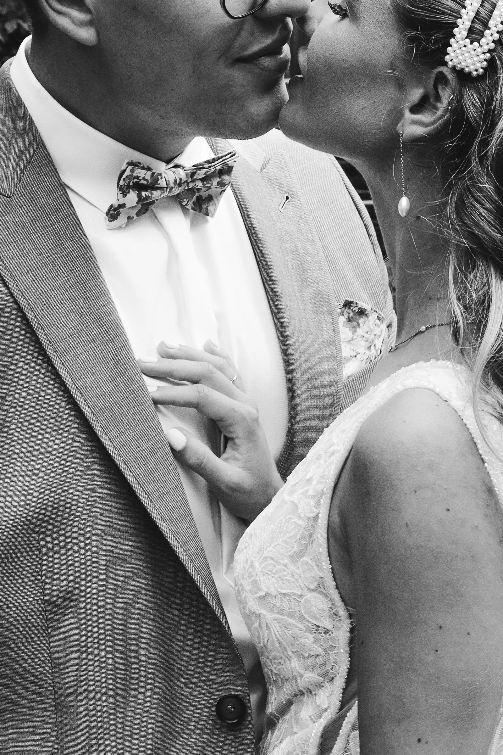 Ein Brautpaar küsst sich bei ihrer Hochzeit, sie trägt ein Spitzenhochzeitskleid und Schmuck, er einen Anzug mit Fliege.