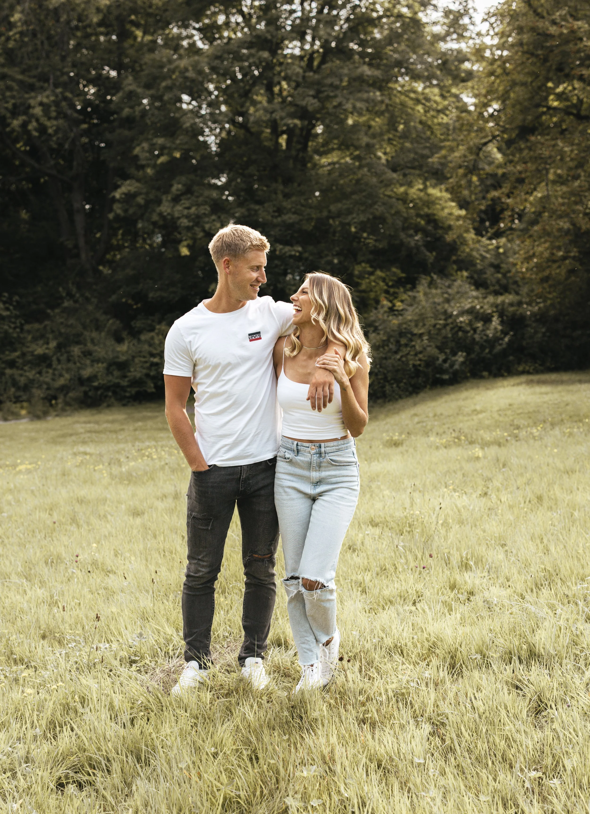 Ein junges Paar spaziert lachend in einem Park bei Sonnenuntergang.