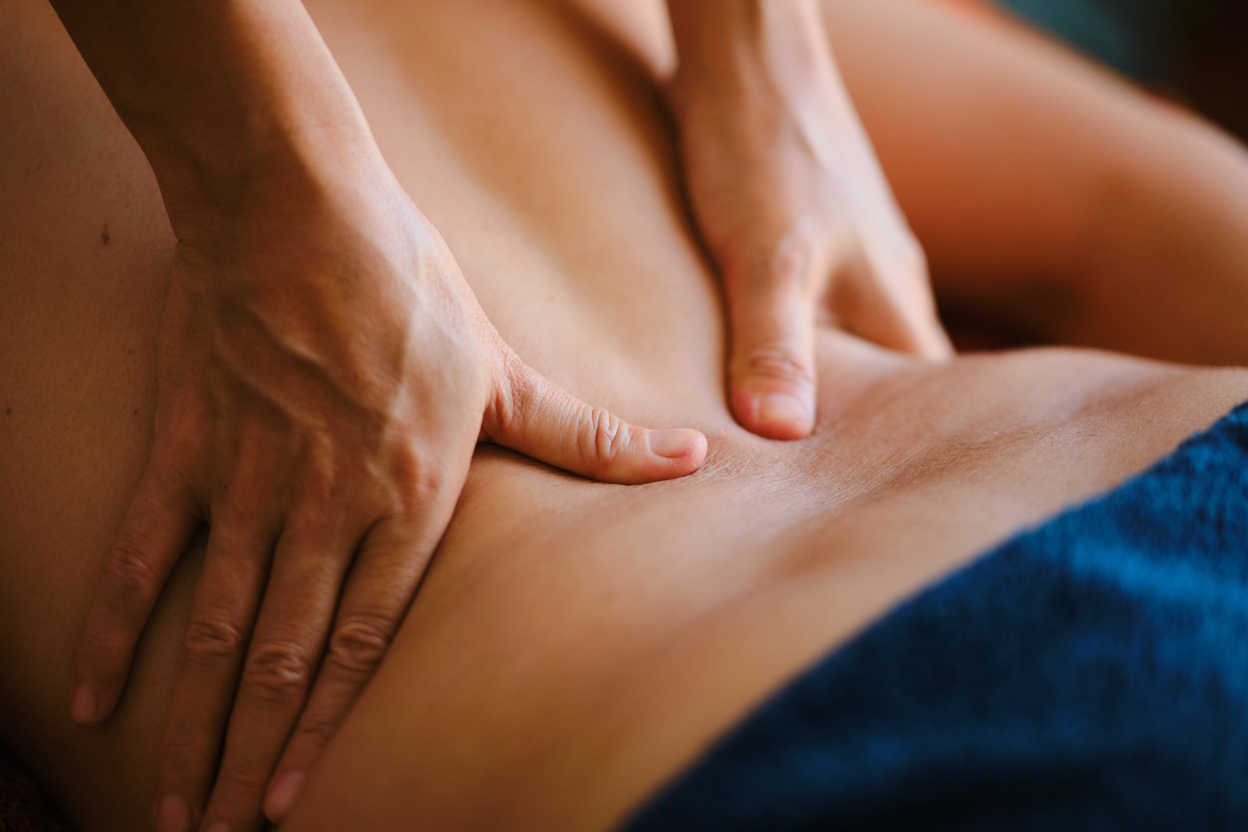 Close-up of a person receiving a massage on their back, with hands applying pressure, in a warm, softly-lit environment.
