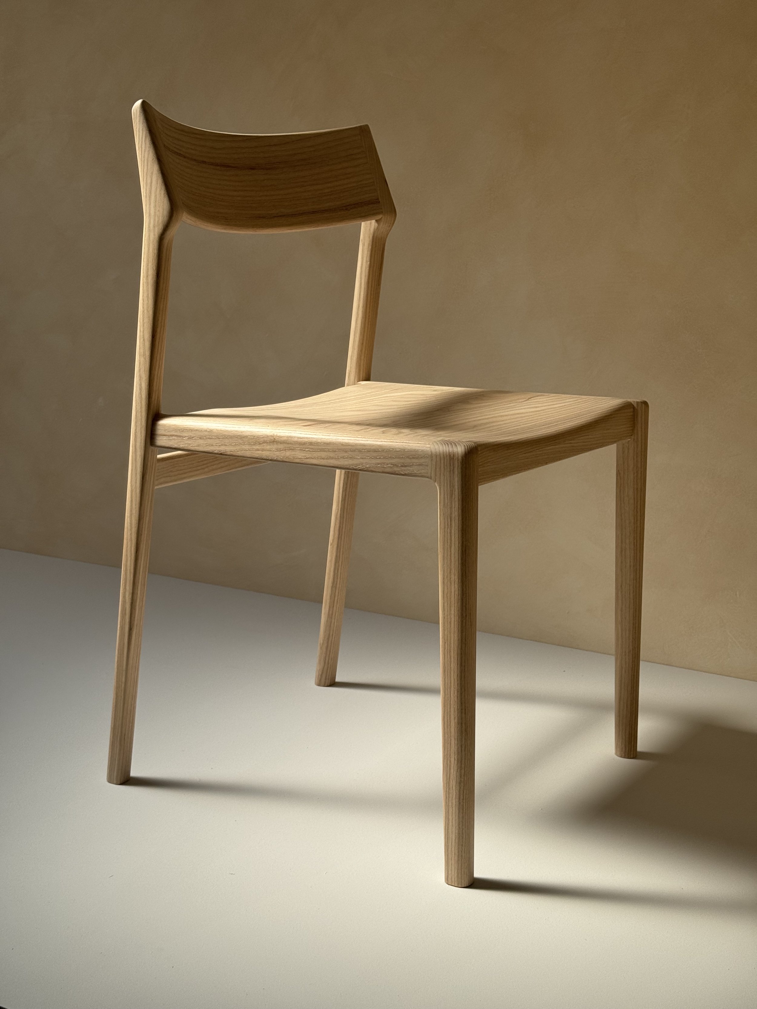 Eleven Chair by Mitch Polley Design, shown from a front angle. A contemporary dining chair with a curved backrest and scooped seat, handmade in English ash.