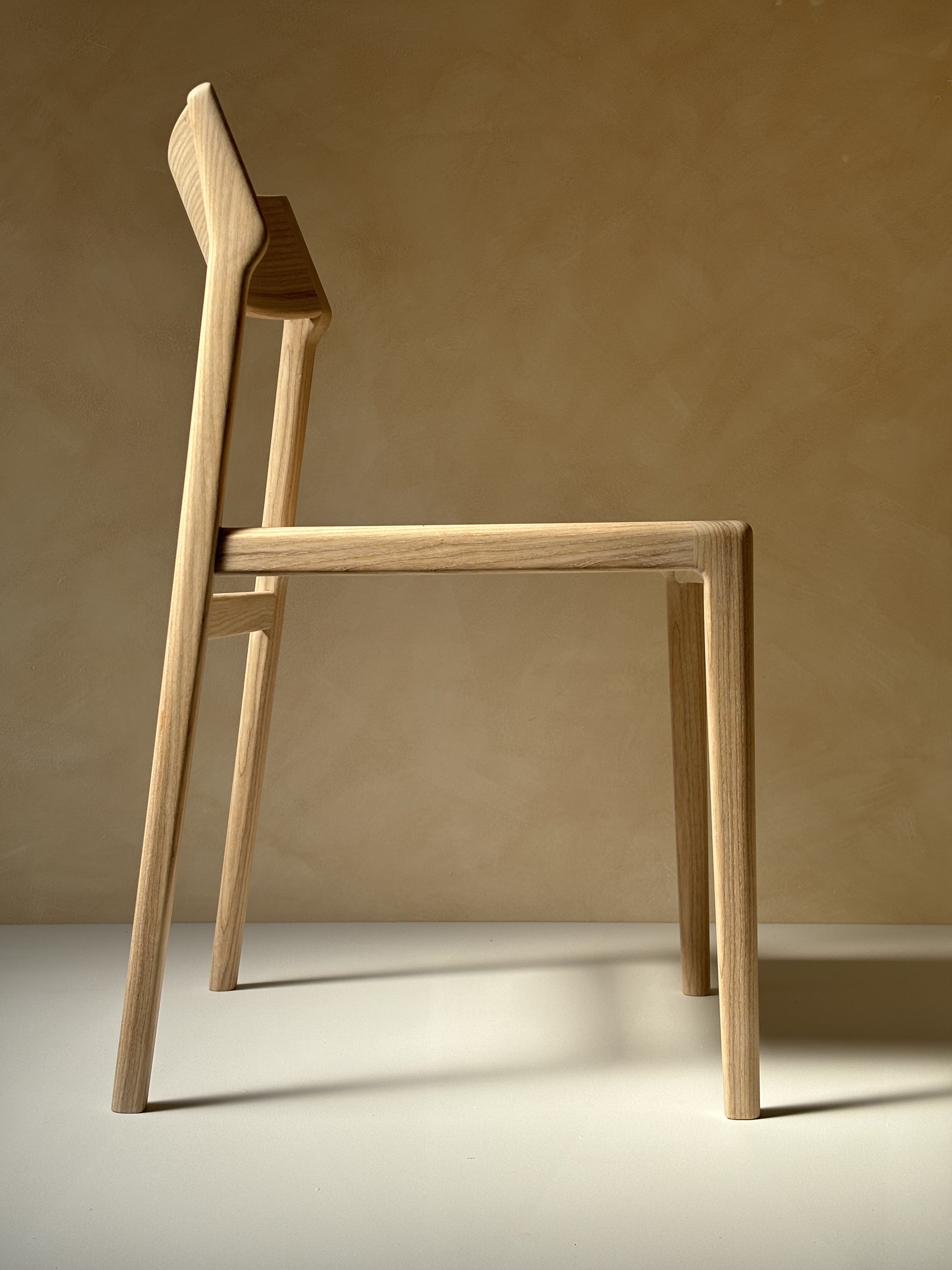 Eleven Chair by Mitch Polley Design, shown from a side angle. A contemporary dining chair with a curved backrest and scooped seat, handmade in English ash.