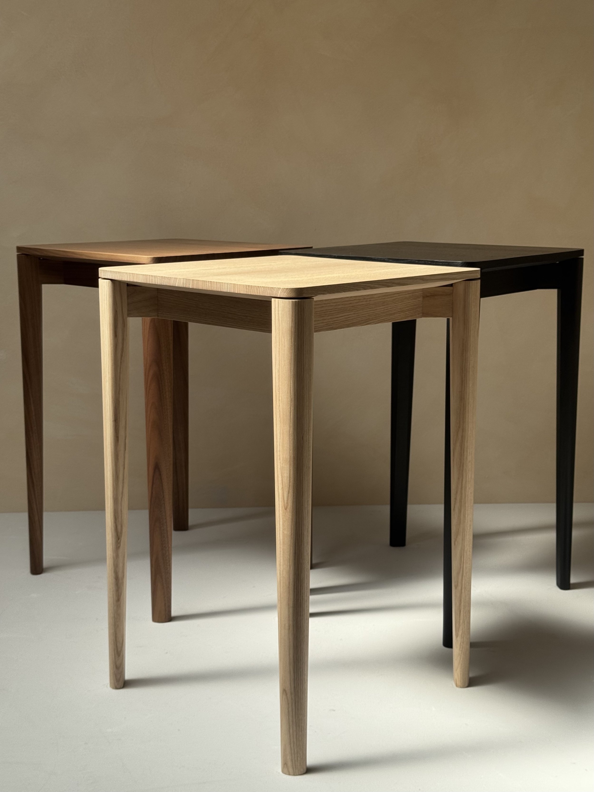 June Table by Mitch Polley Design, shown from front angle in front of Walnut and Ebonised Ash versions of the same piece. A minimalist side table with clean lines, handmade from English Ash.
