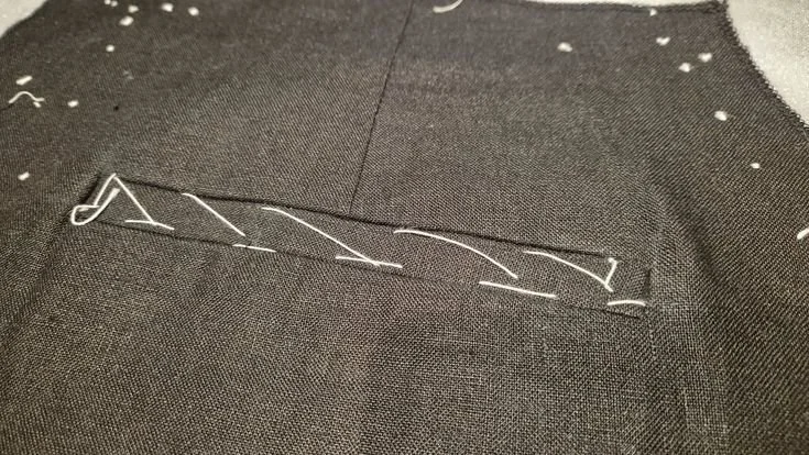 Close-up of a brown fabric with a pocket stitched with white thread.