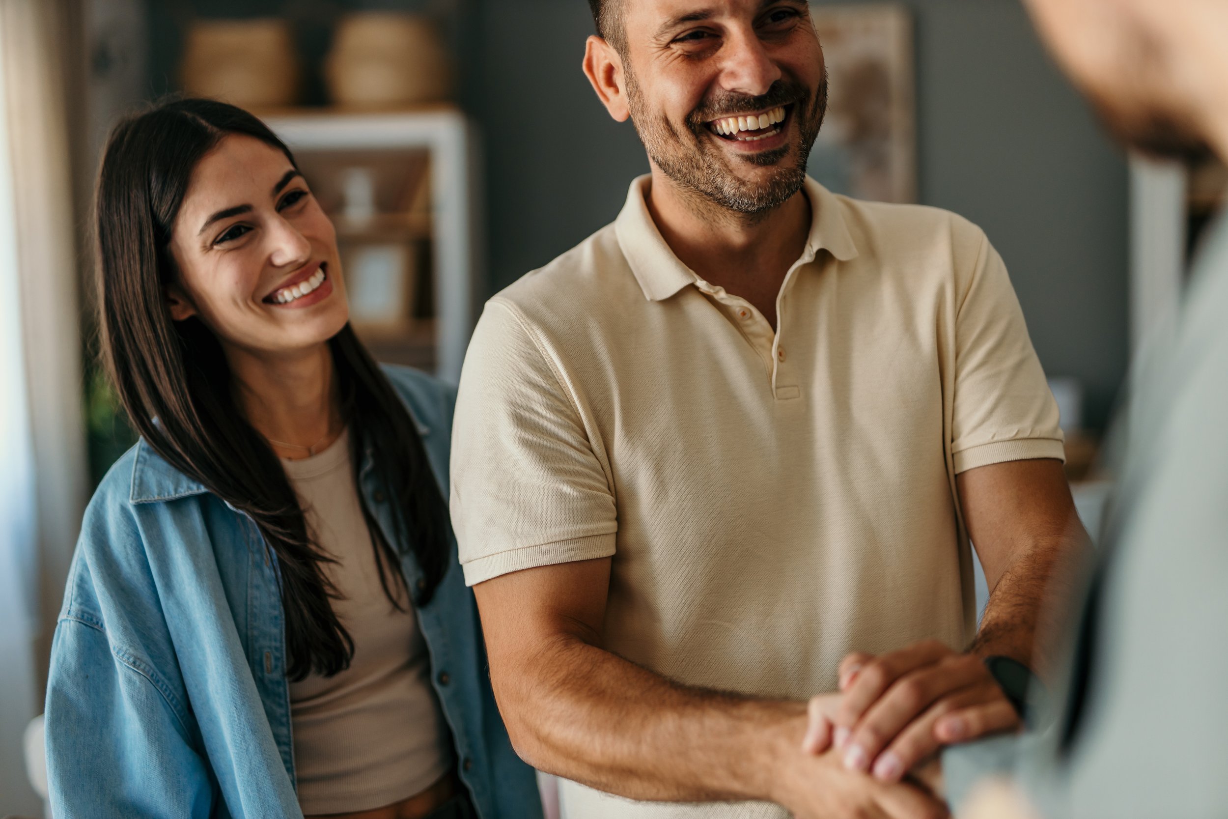 Two smiling adults, a man and a woman, engaging with another person in a casual setting.