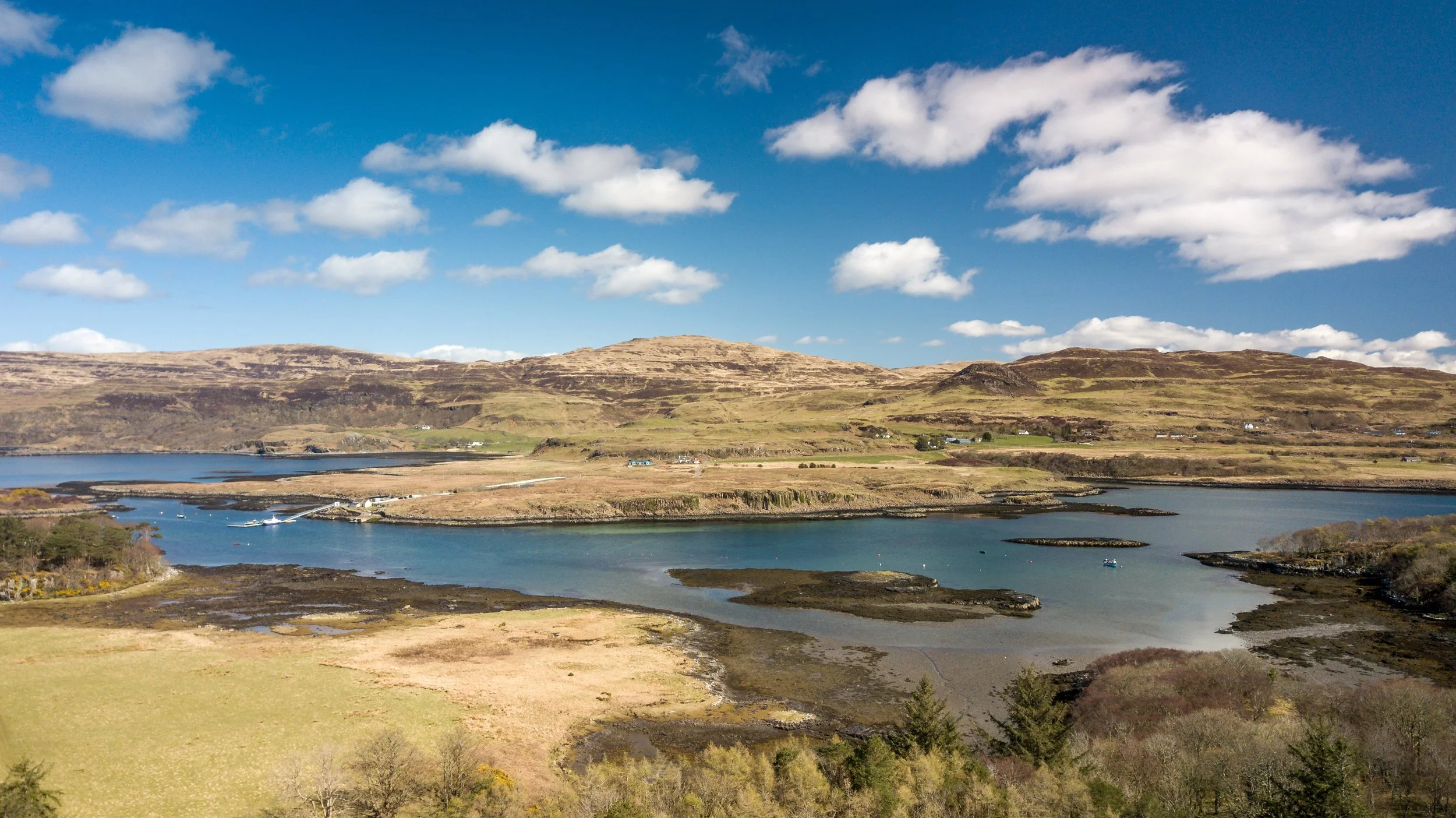 Landscape of a coastal area with hills, water, boats, and a partly cloudy sky.